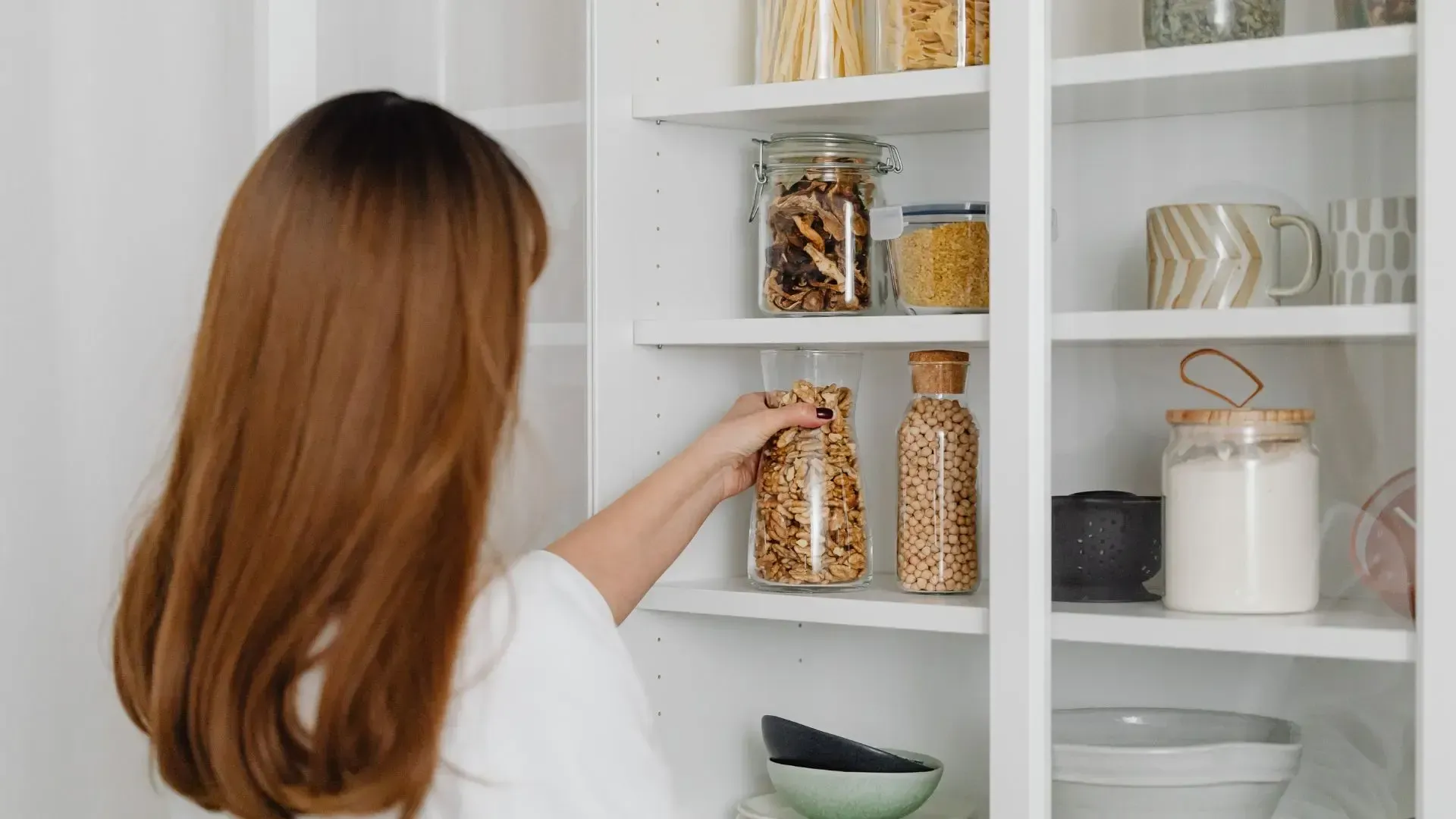 A woman is taking a jar out of a pantry.