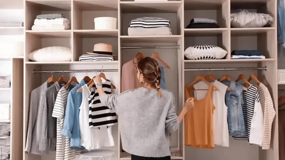 Person organizing clothes in a built-in closet with folded items and hanging shirts.