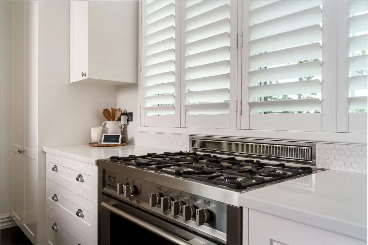 A kitchen with a stove and shutters on the windows.