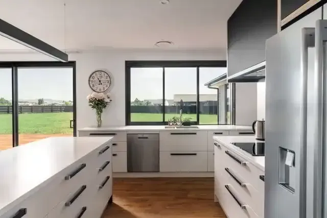 A kitchen with white cabinets , stainless steel appliances and a clock on the wall.