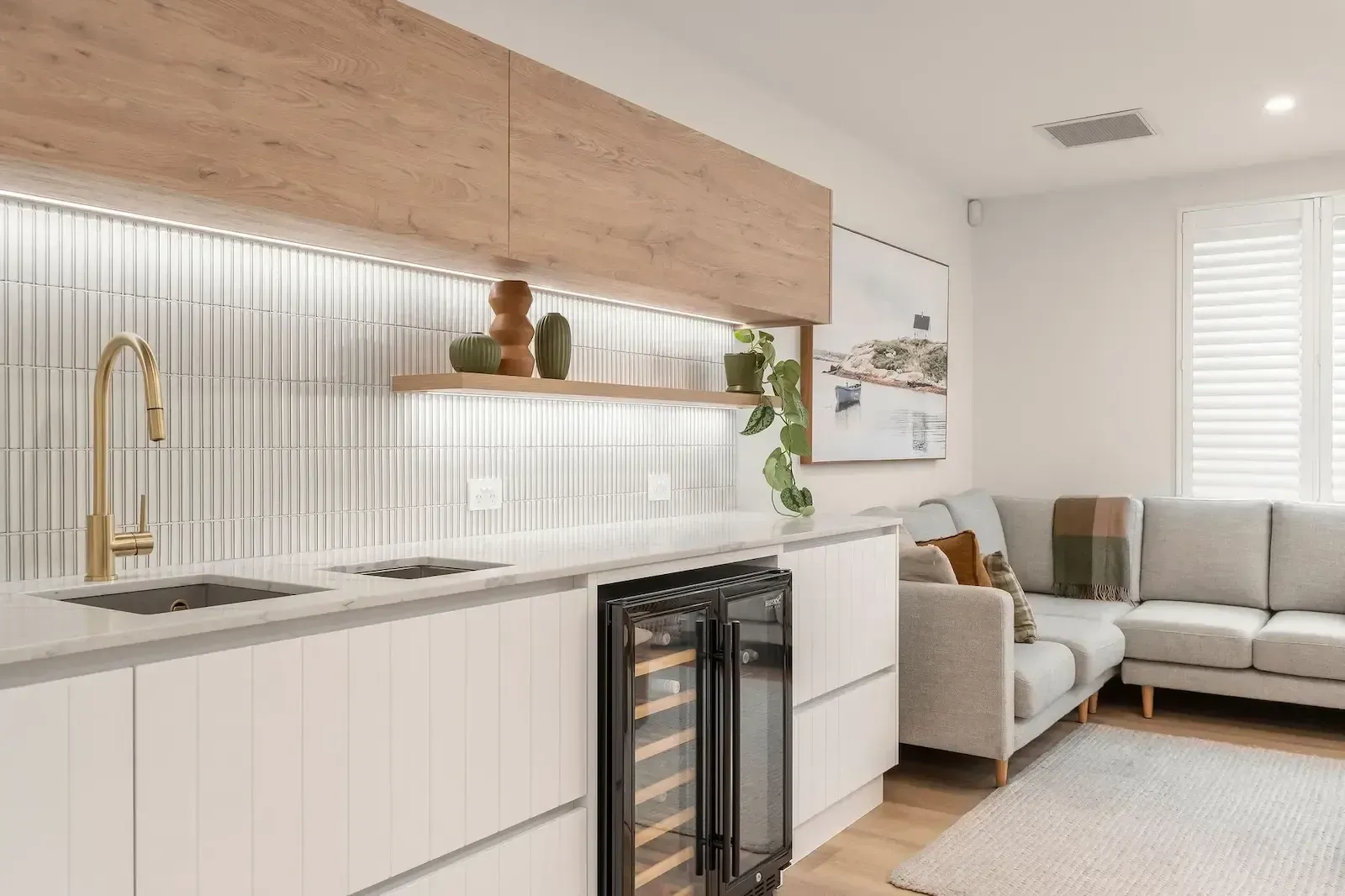 A living room with a couch and a kitchen with a wine cooler.