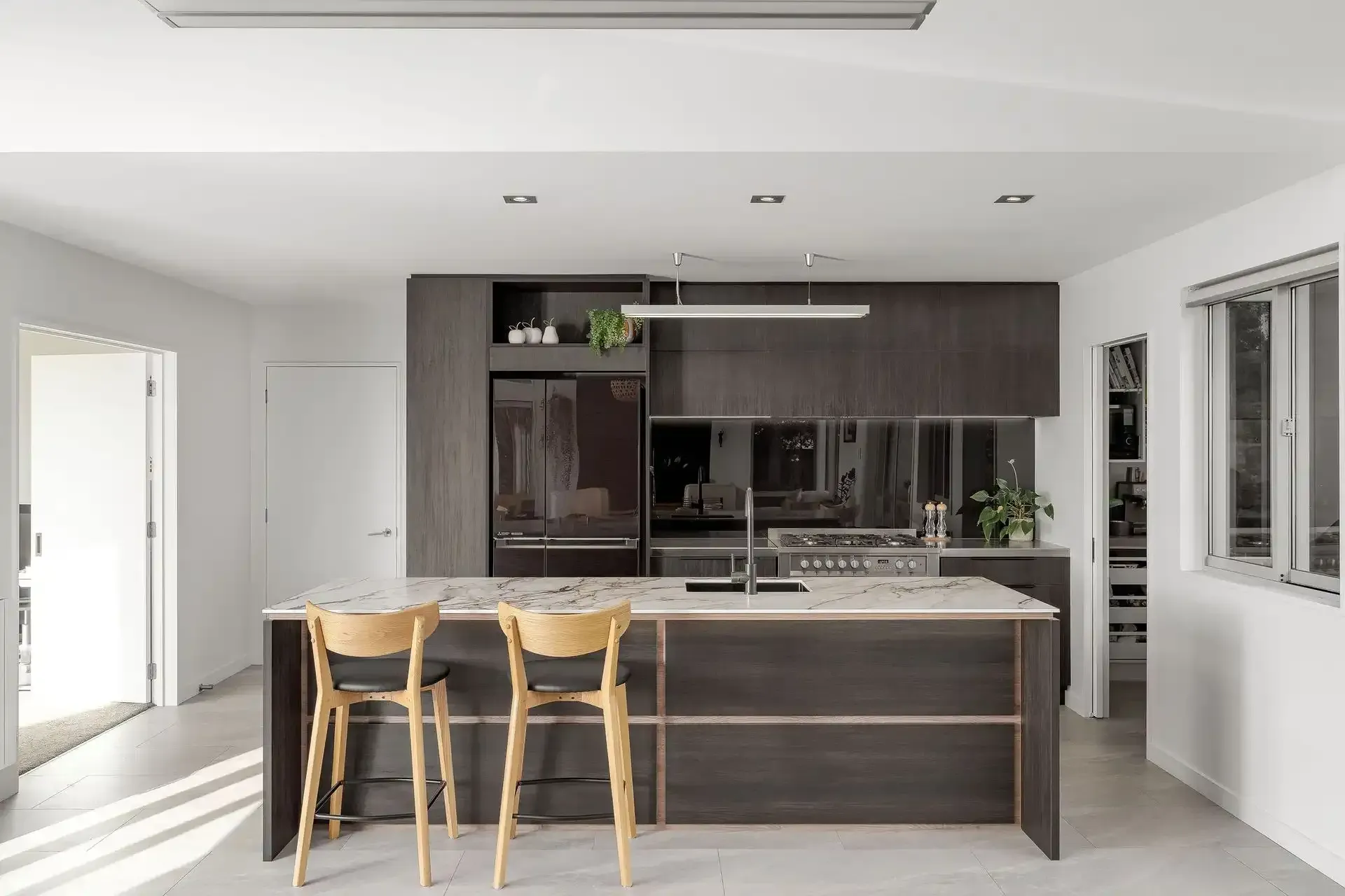 Modern kitchen with dark wood cabinets, island, two stools, and bright white walls and windows