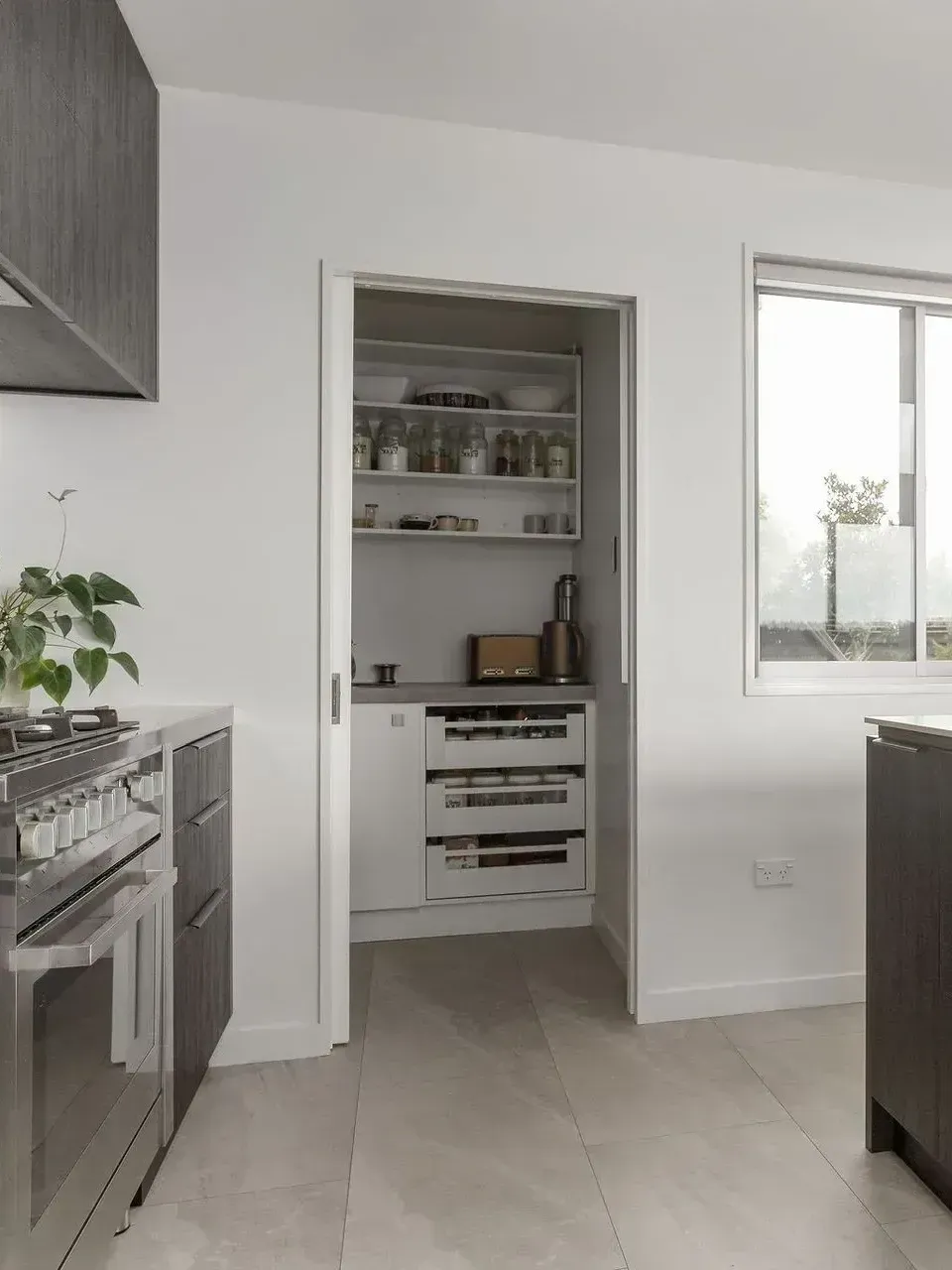 Modern kitchen with white cabinets, built-in oven, open pantry, and a window.