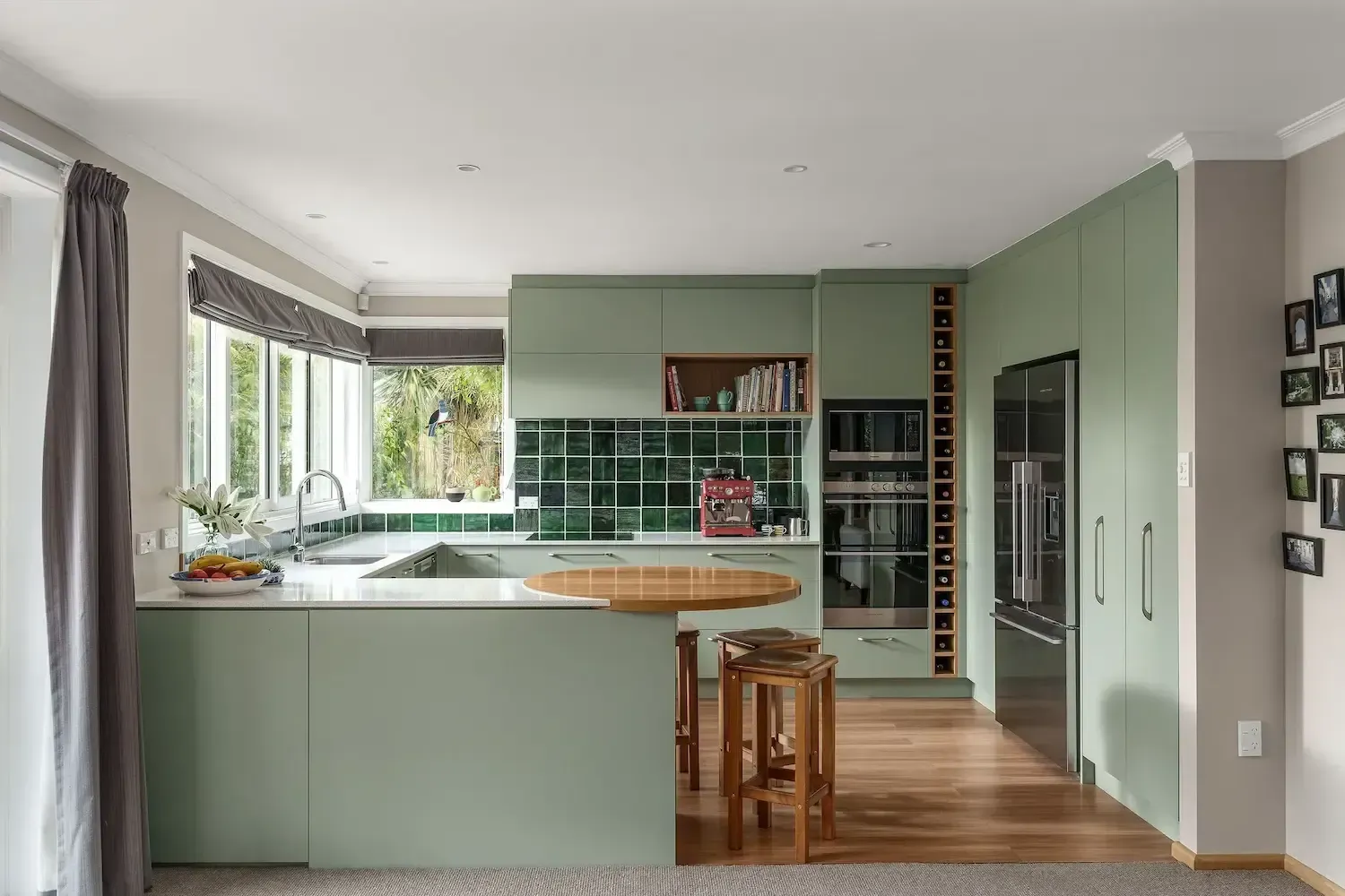 A kitchen with green cabinets , stainless steel appliances , a table and stools.
