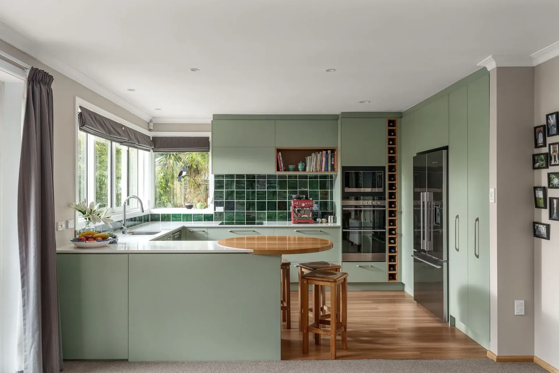 A kitchen with green cabinets , stools , a refrigerator and a sink.