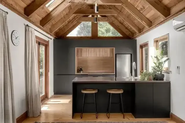 Modern cabin kitchen with wood-beamed ceiling, black island stools, and large windows