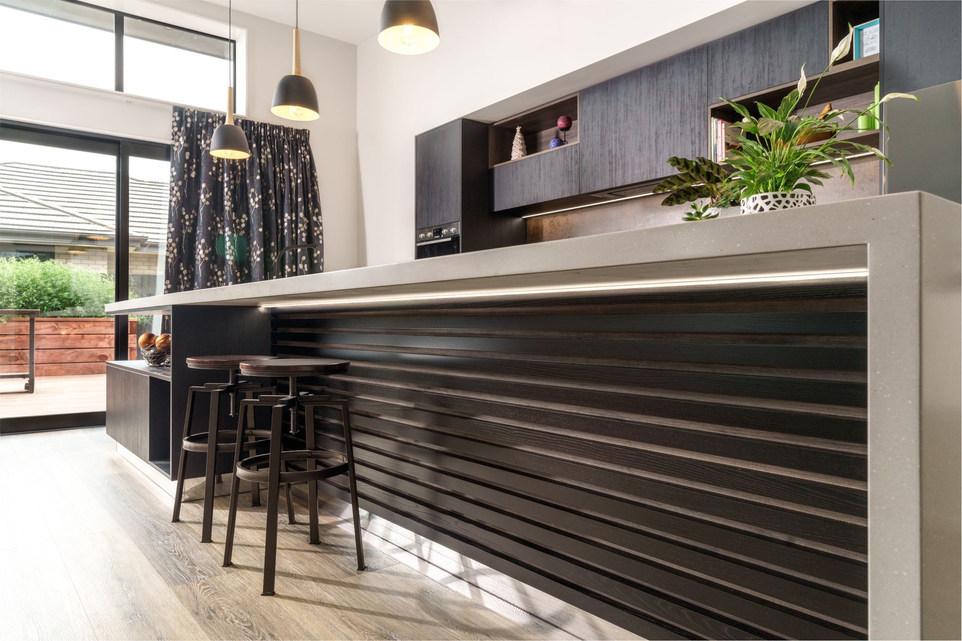 A kitchen with a long counter and stools and a sliding glass door.