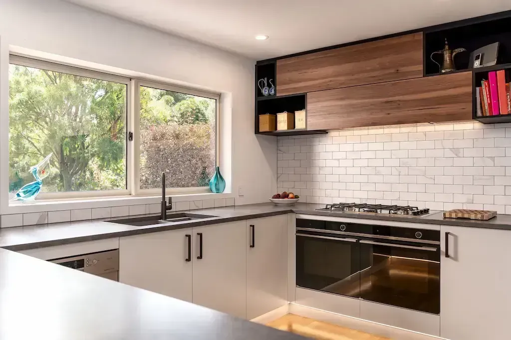 A kitchen with white cabinets , black appliances and a large window.