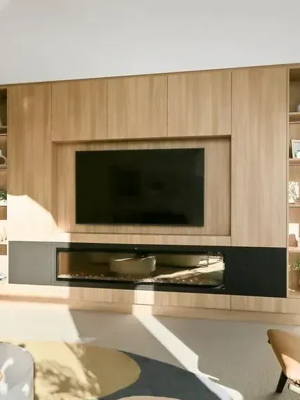 Modern wall-mounted TV with wooden cabinetry and a fireplace beneath in a bright living room