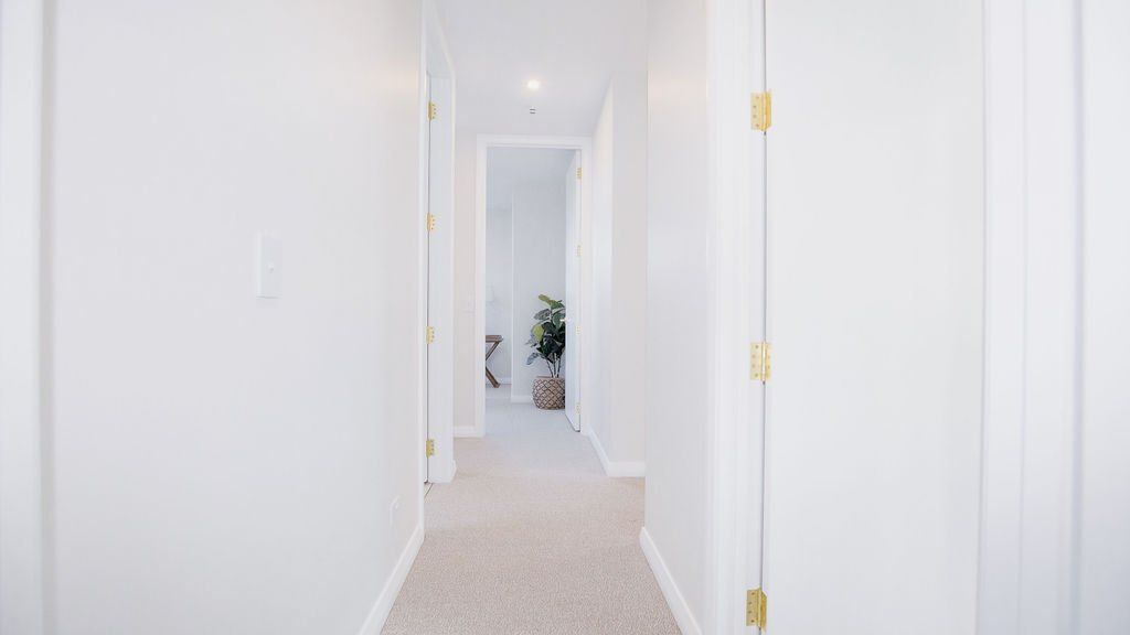 A long hallway in a house with white walls and carpet.