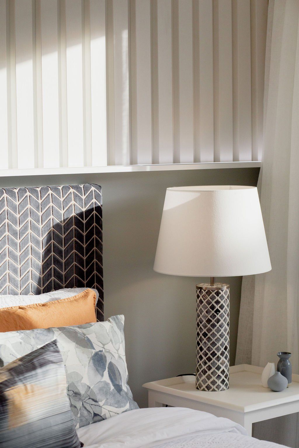 A bedroom with a bed , nightstand , lamp and curtains.
