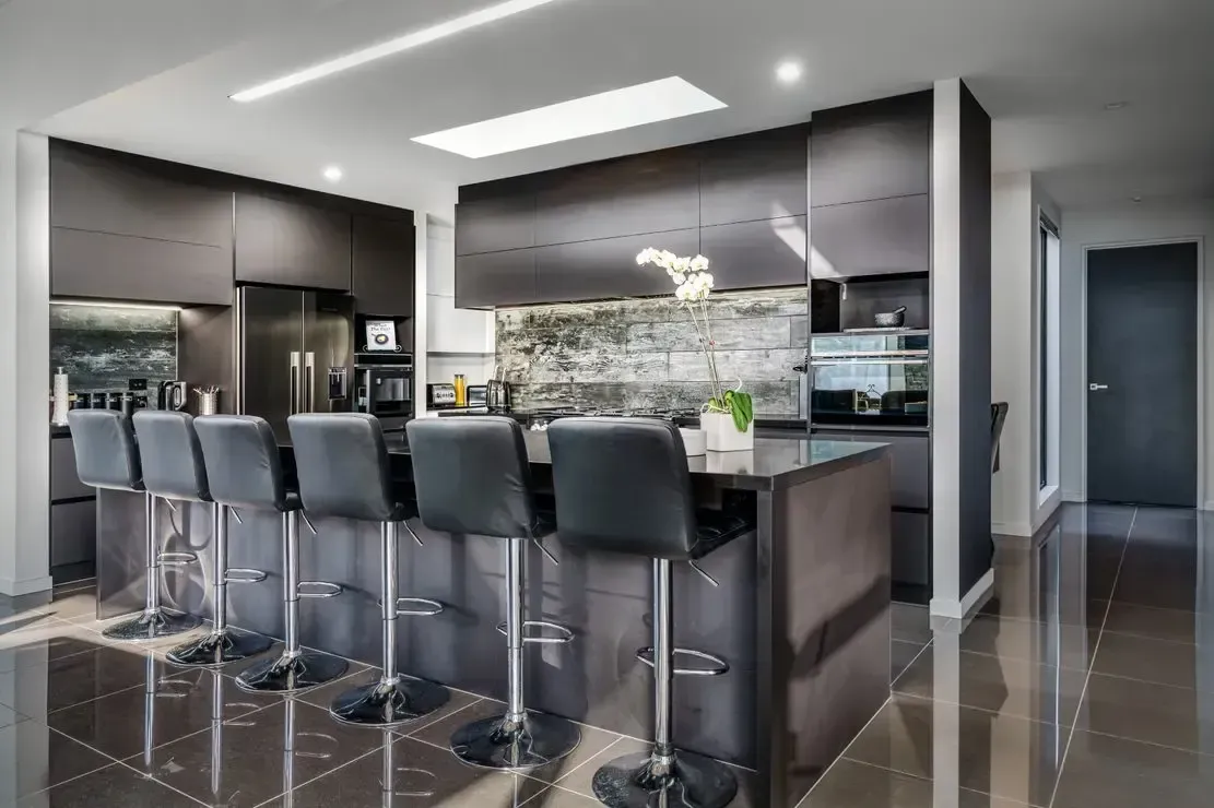 A kitchen with black cabinets and stools and a large island.