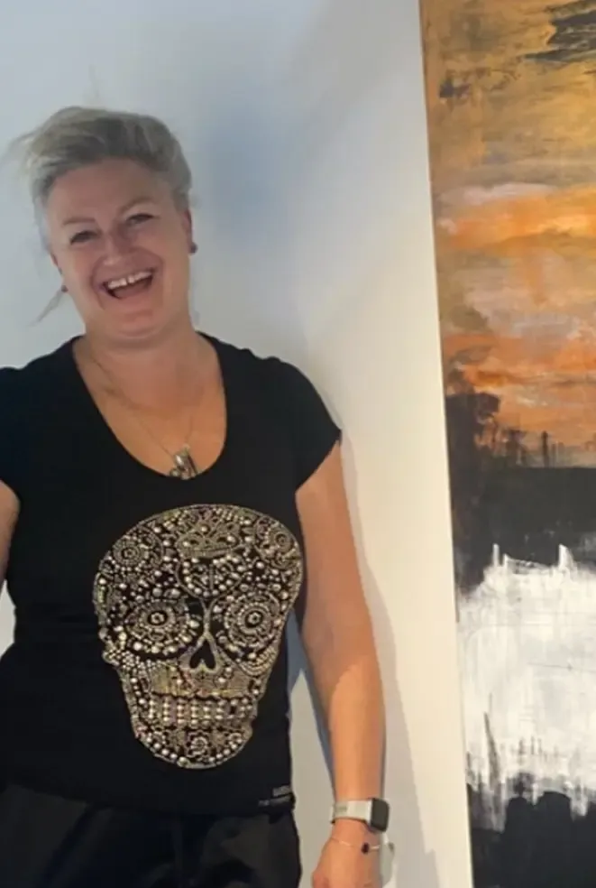 Smiling person in a black skull T-shirt standing beside abstract wall art.