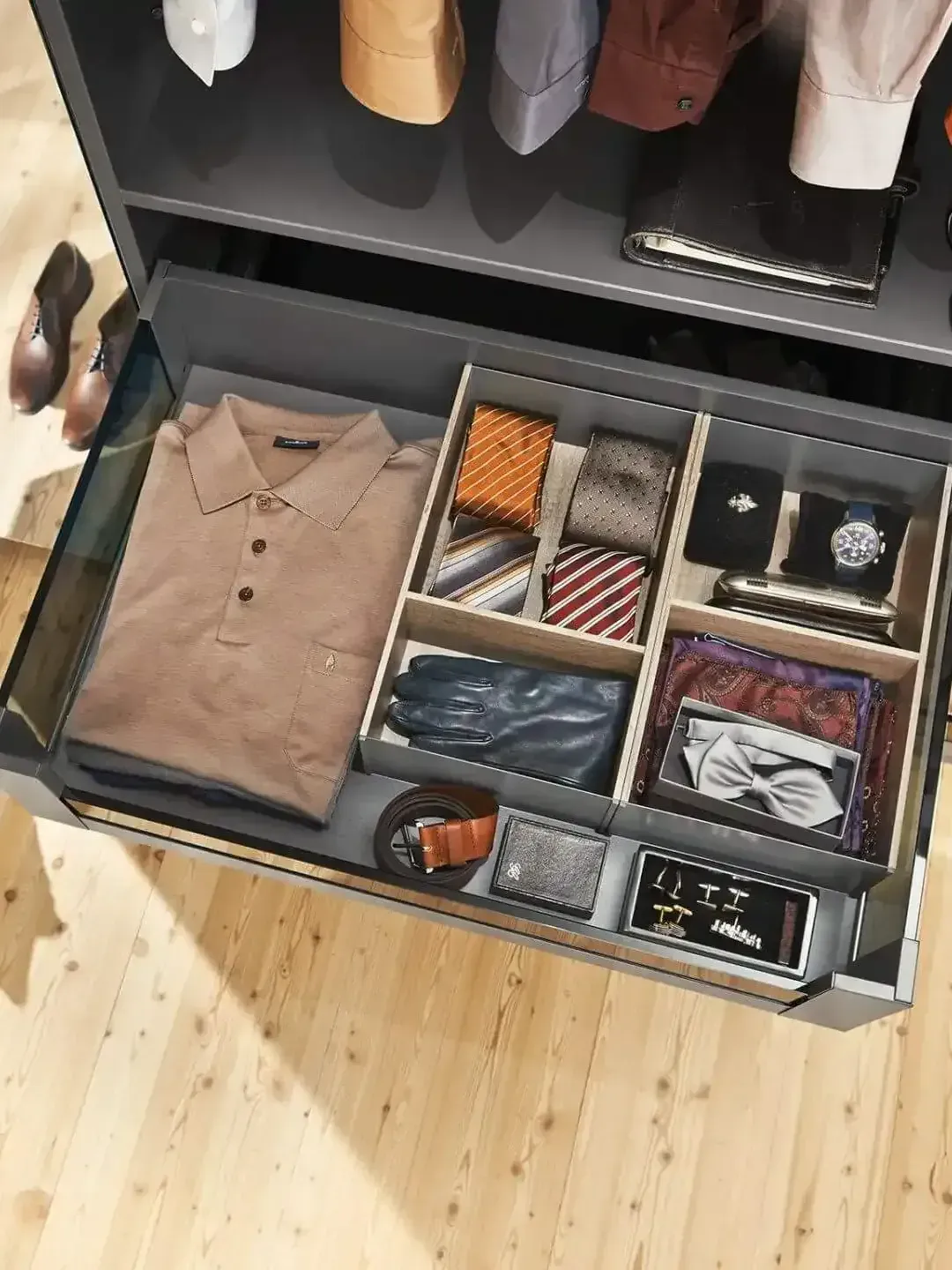 Open drawer of neatly organized men’s accessories and folded shirts in a closet.
