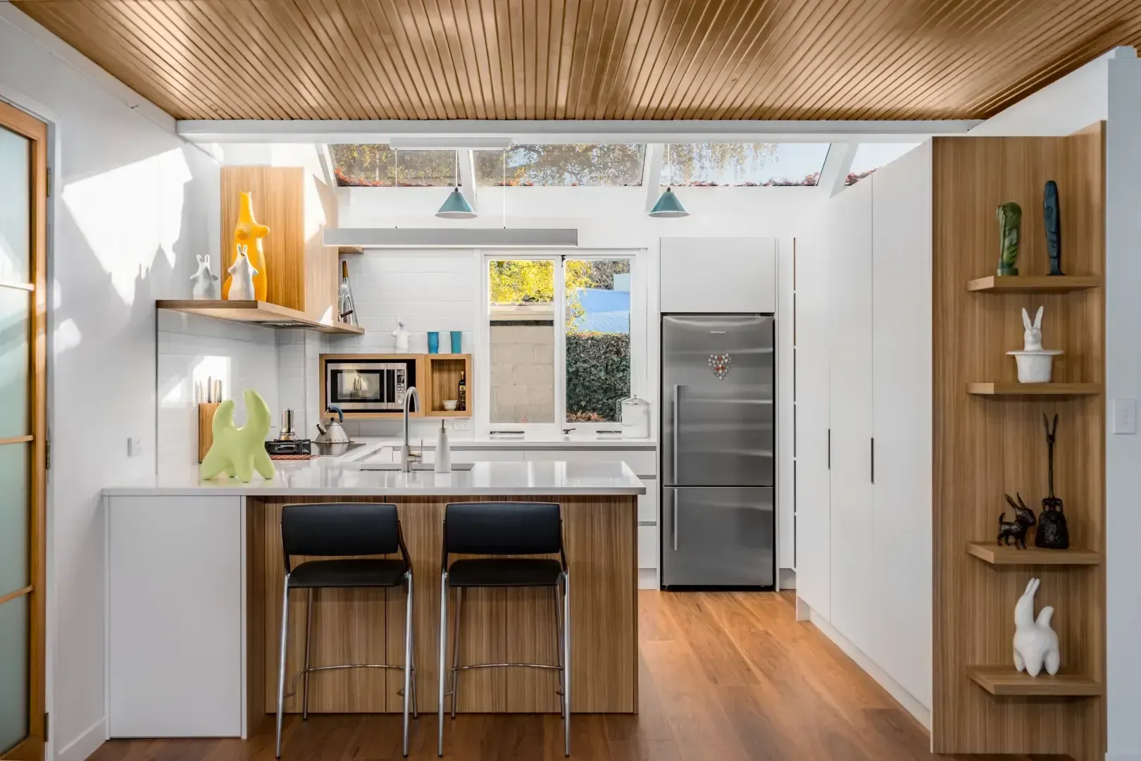 A kitchen with white cabinets , wooden floors , stools and a refrigerator.