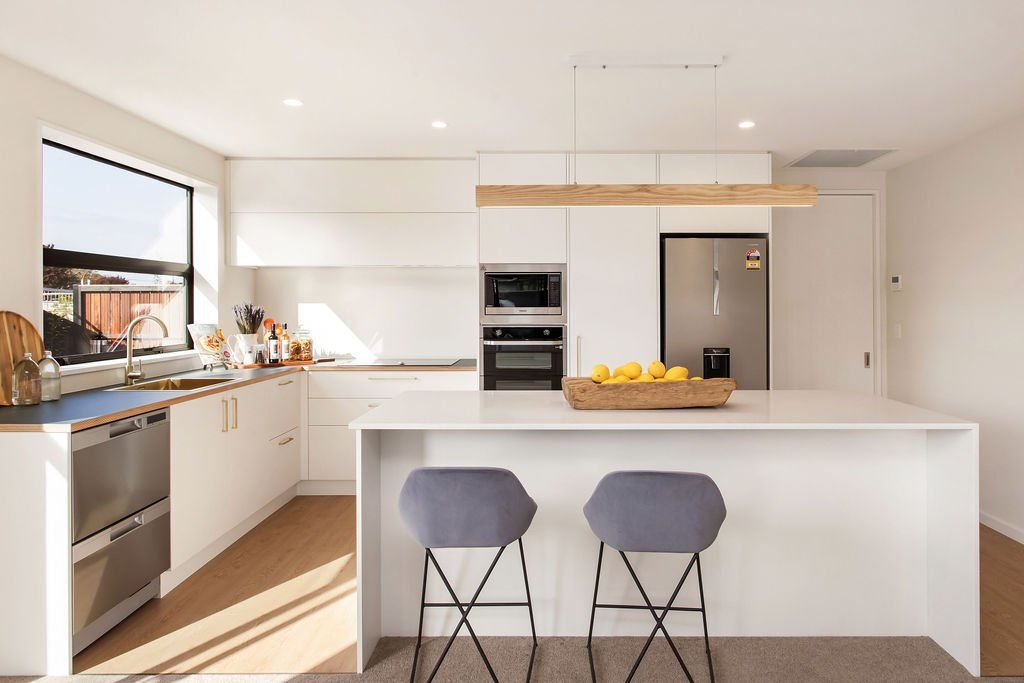 A kitchen with white cabinets , stainless steel appliances , a large island and two stools.