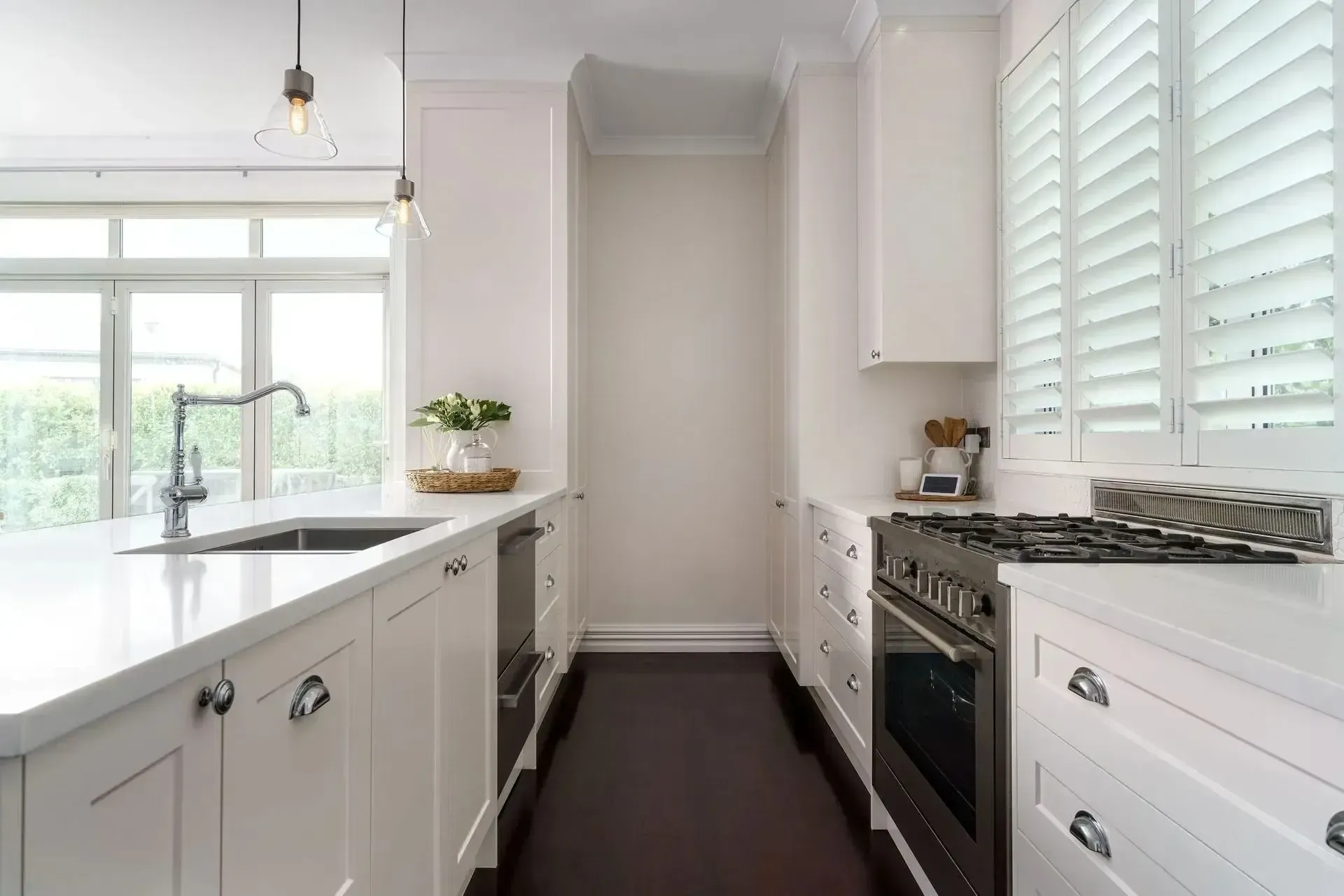 White kitchen with a long island, dark floor, and oven against the wall with shutters.