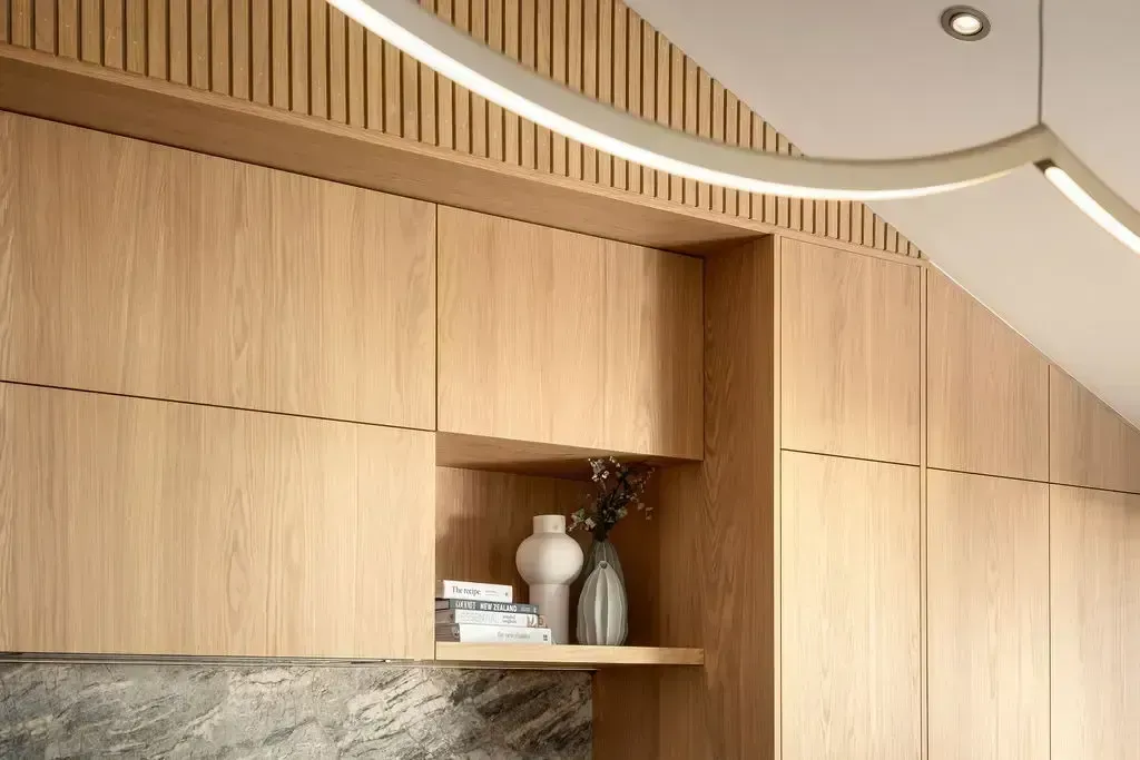 Wooden cabinetry with recessed shelf holding vases and books, lit by a curved light fixture.