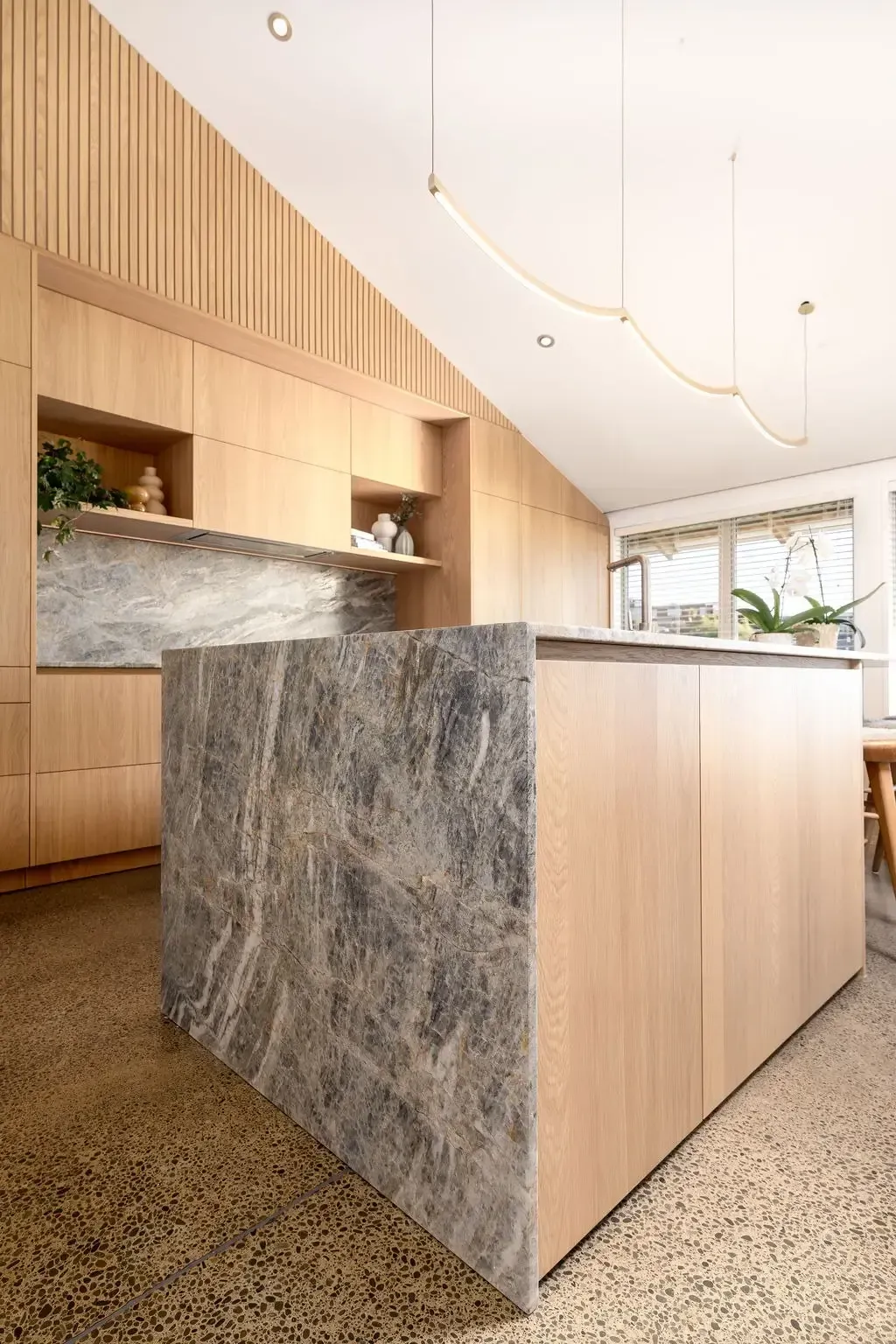 Modern kitchen with wood cabinets, gray marble island, light fixture, and terrazzo flooring.