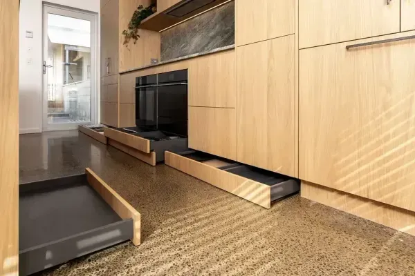 Kitchen with light wood cabinets, open drawers, and a polished concrete floor.