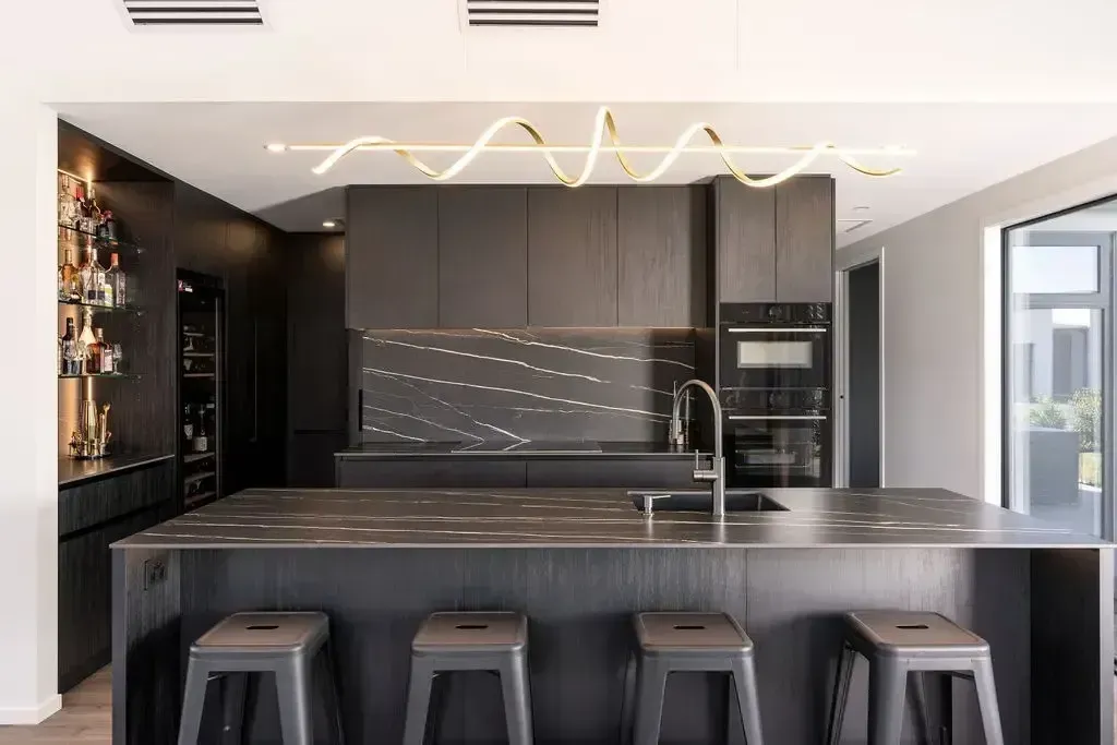 Modern kitchen with black cabinets, island, and stools, illuminated by a curved light fixture.