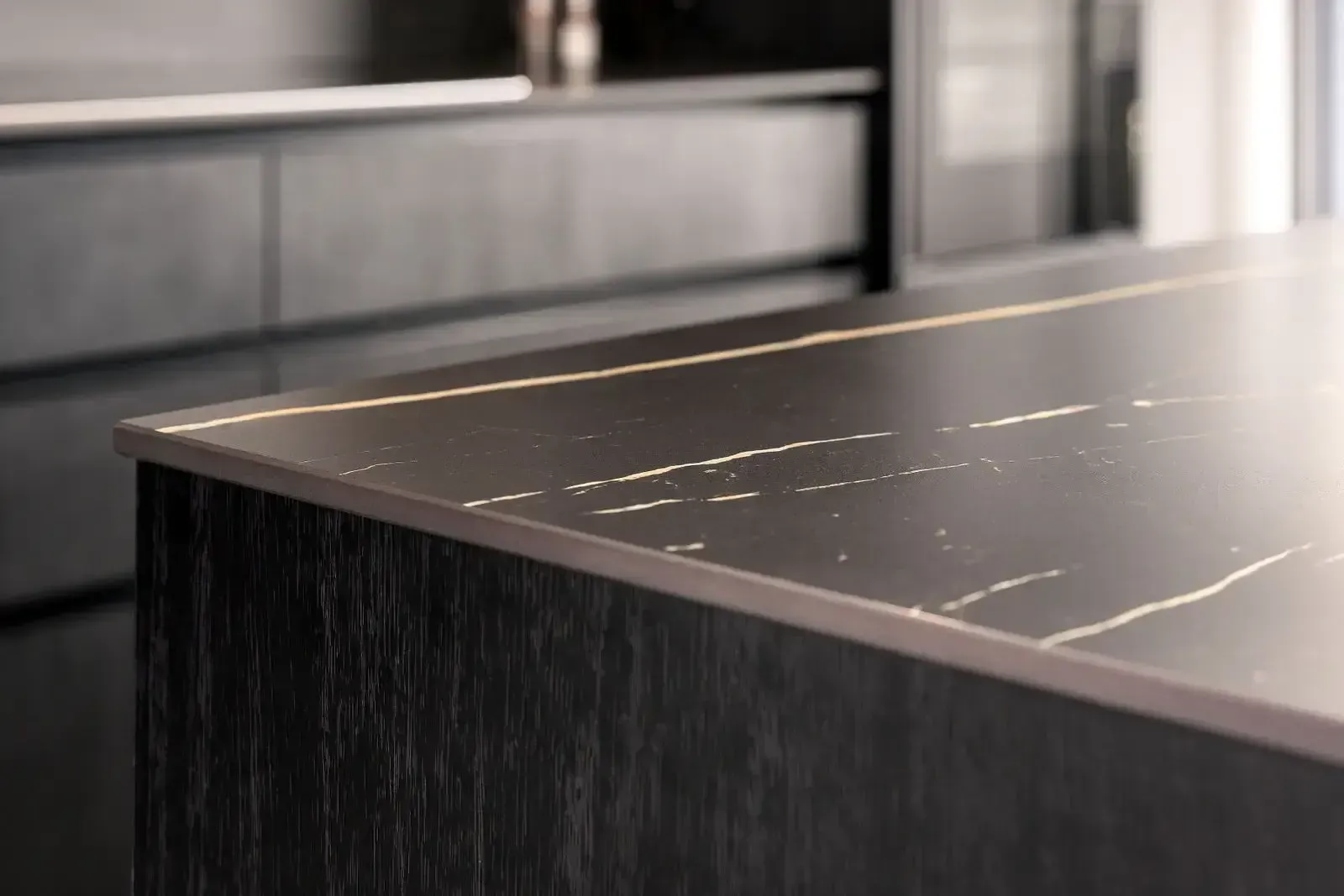 Close-up of a dark kitchen island with a black countertop with gold veining and a metallic edge.