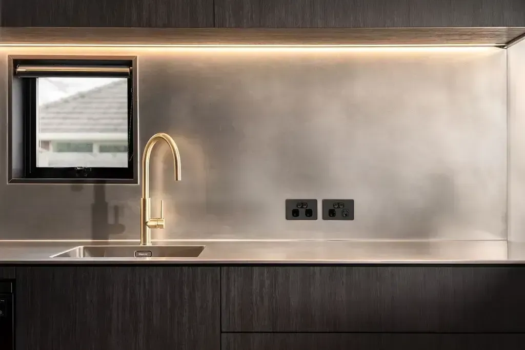 Modern kitchen with gold faucet, metallic backsplash, and dark wood cabinets. Window provides natural light.