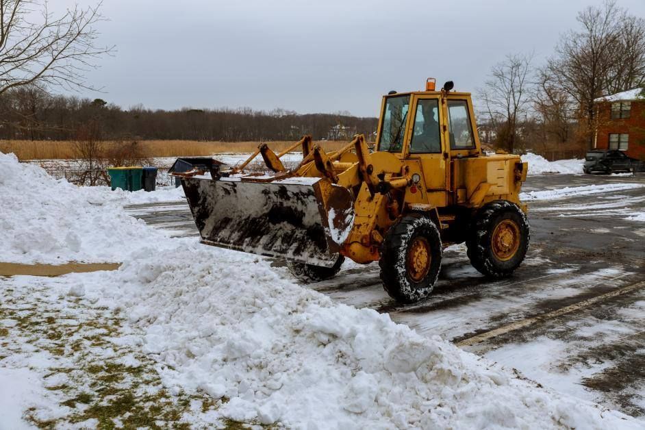A yellow snow plow is clearing snow from a parking lot.