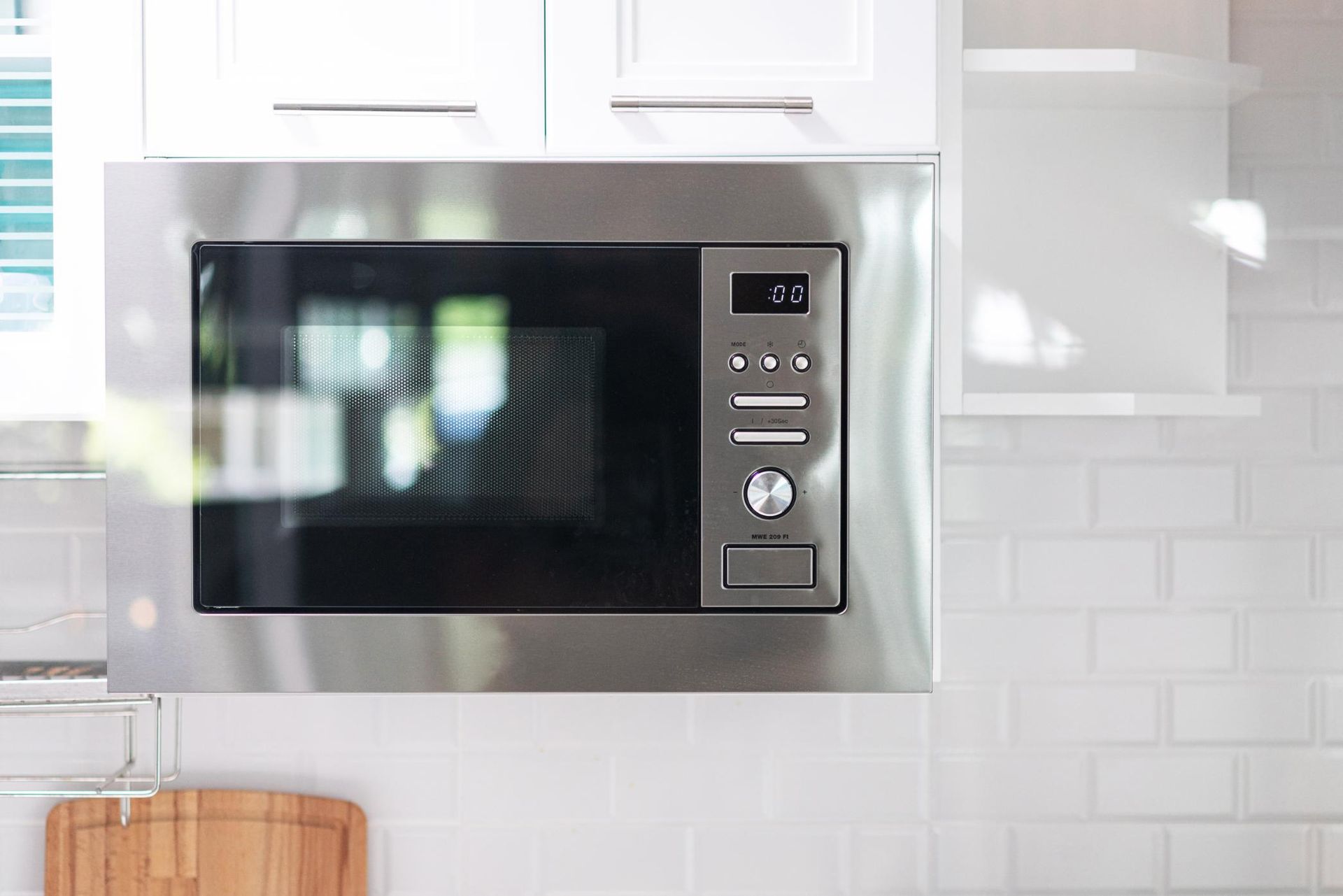 Built-in stainless steel microwave above a white kitchen counter and tiled backsplash
