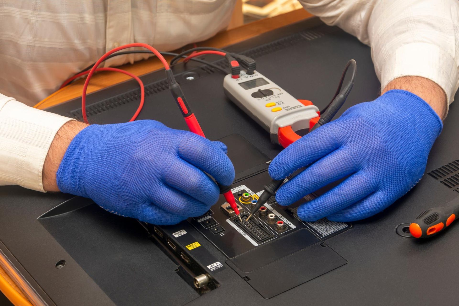 Gloved hands repairing an electronic circuit board with tools on a black work surface.