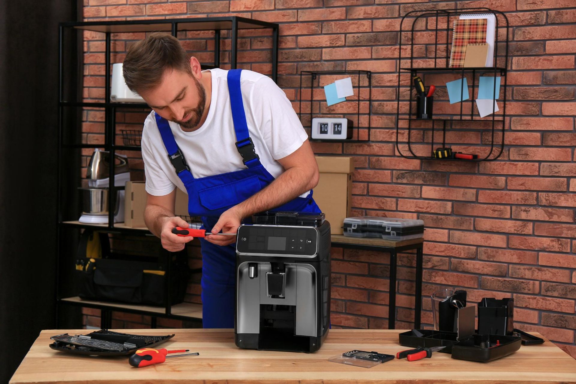 Man in blue overalls repairing a coffee machine on a workbench in a workshop