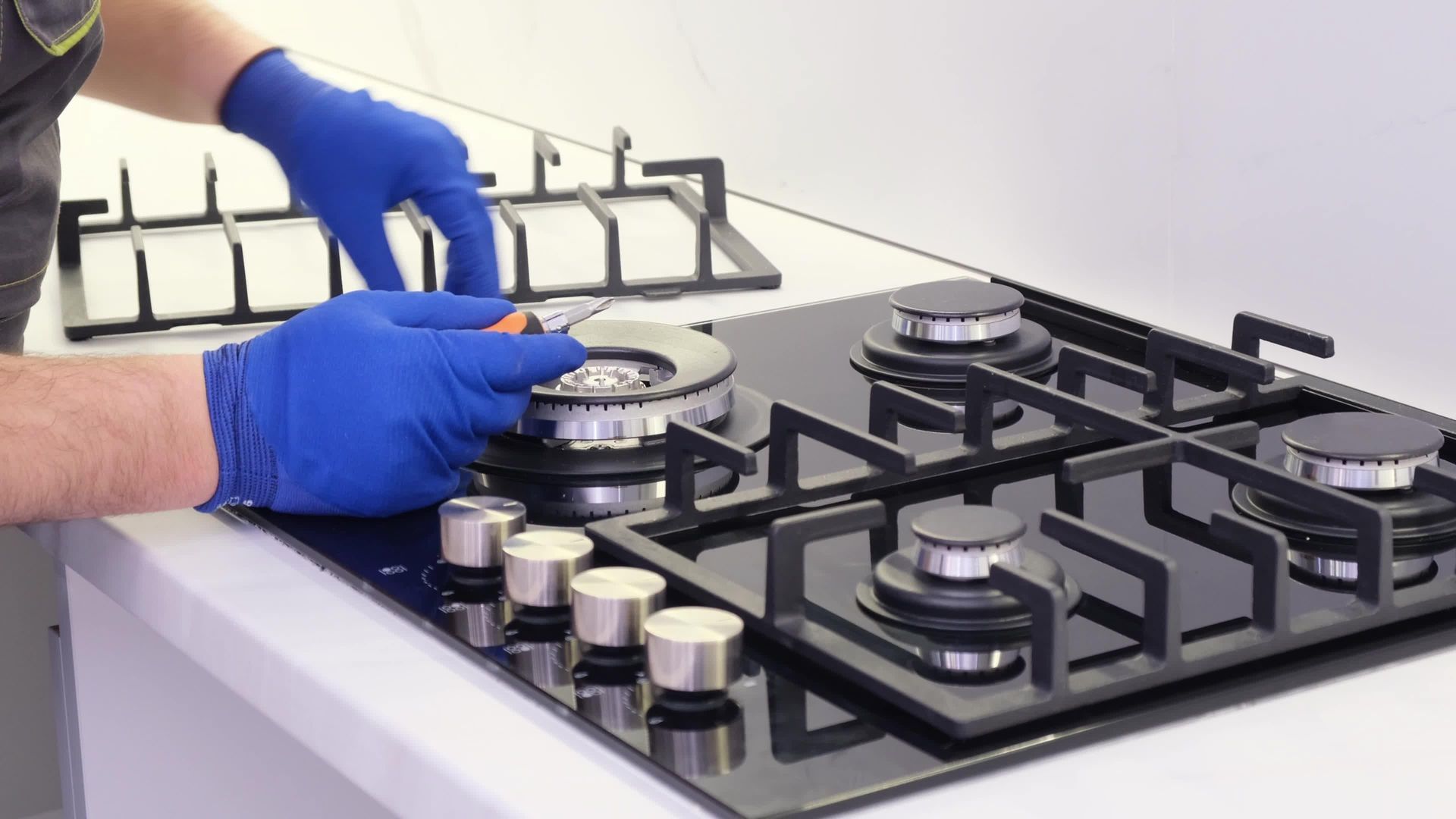 Gloved hands cleaning a black gas stovetop in a bright kitchen
