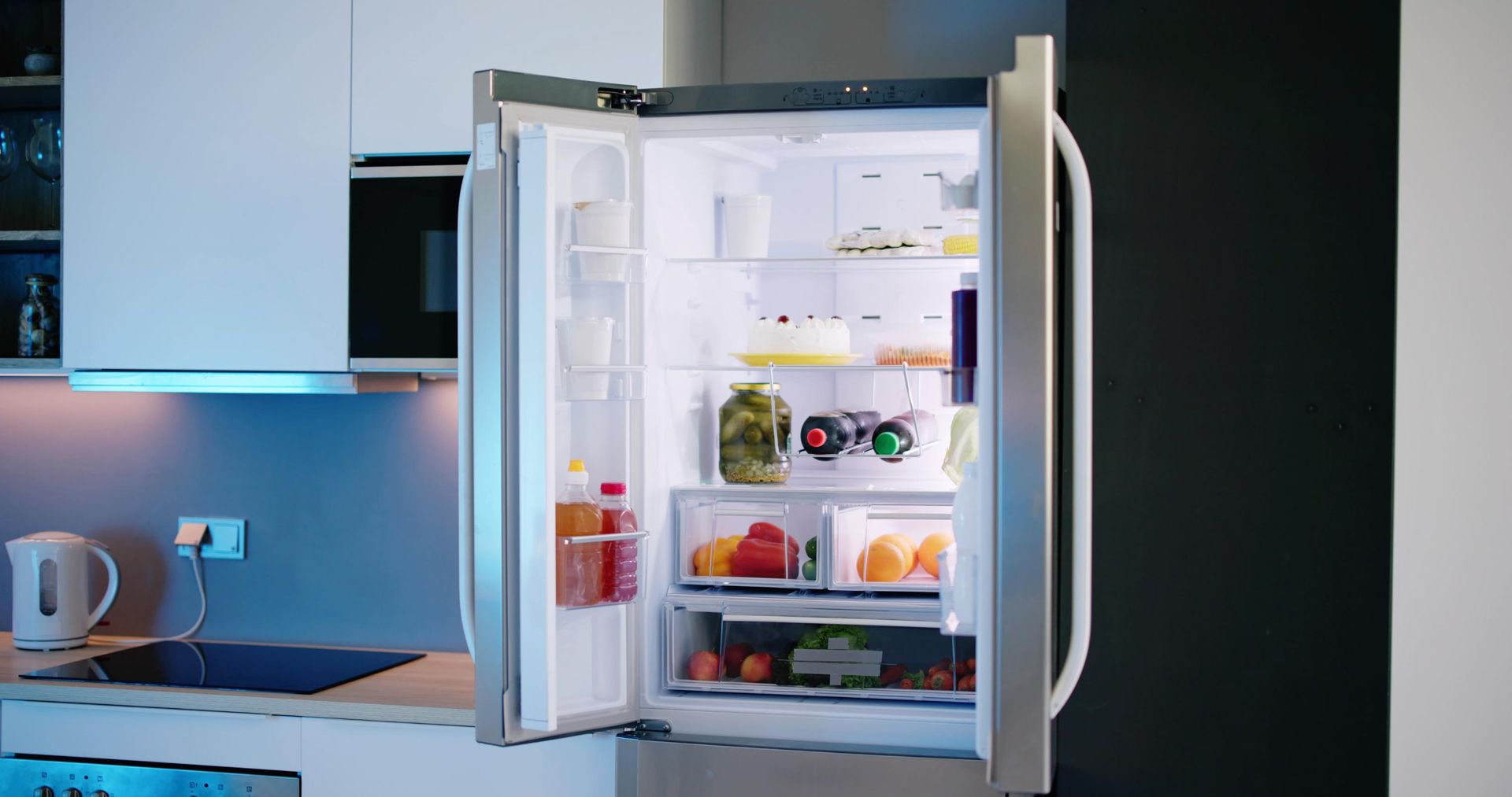 Open refrigerator with milk, fruit, and vegetables in a modern kitchen