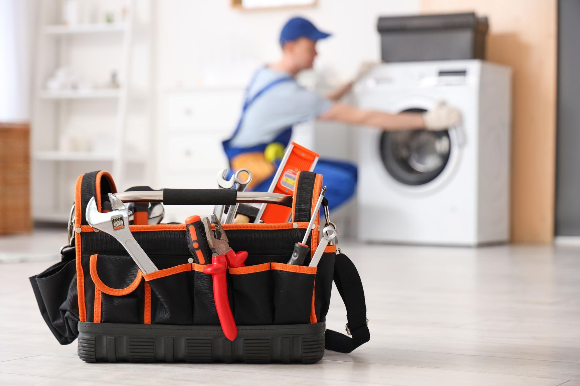 Tool bag in foreground, with a worker in a blue cap washing clothes in a laundry room behind it