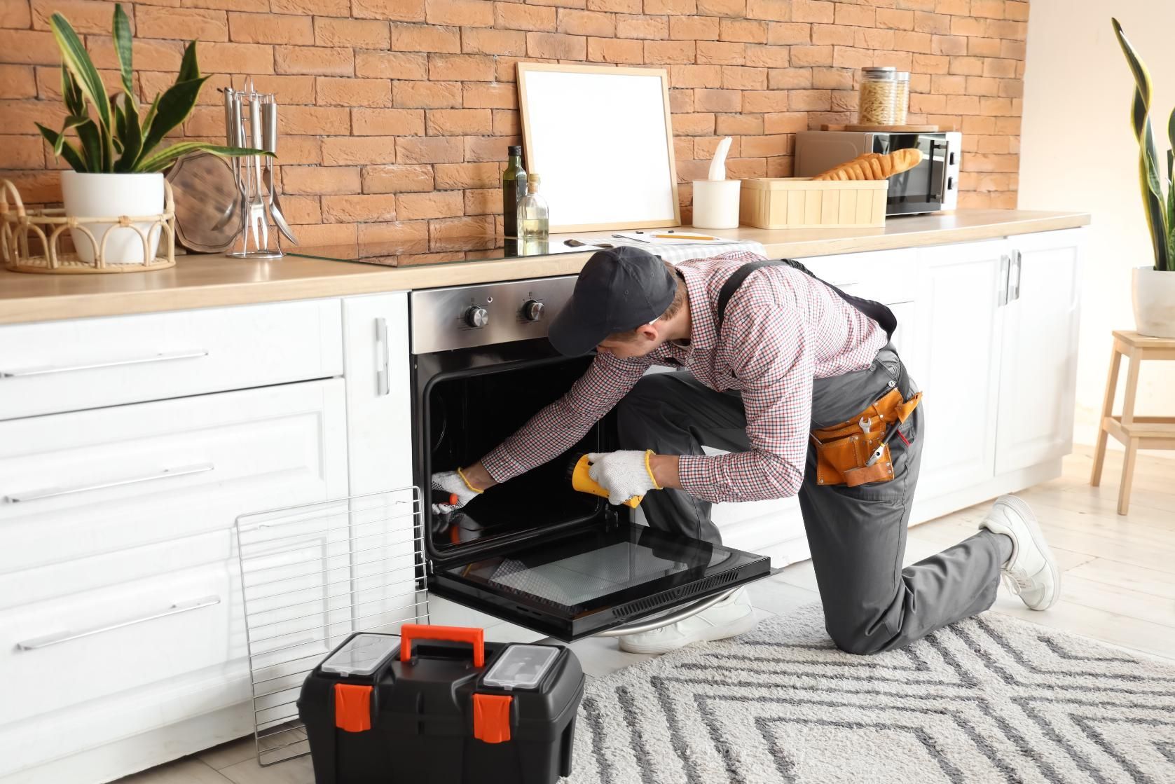 Person kneeling at an open oven door in a bright kitchen, using a yellow cleaning cloth.