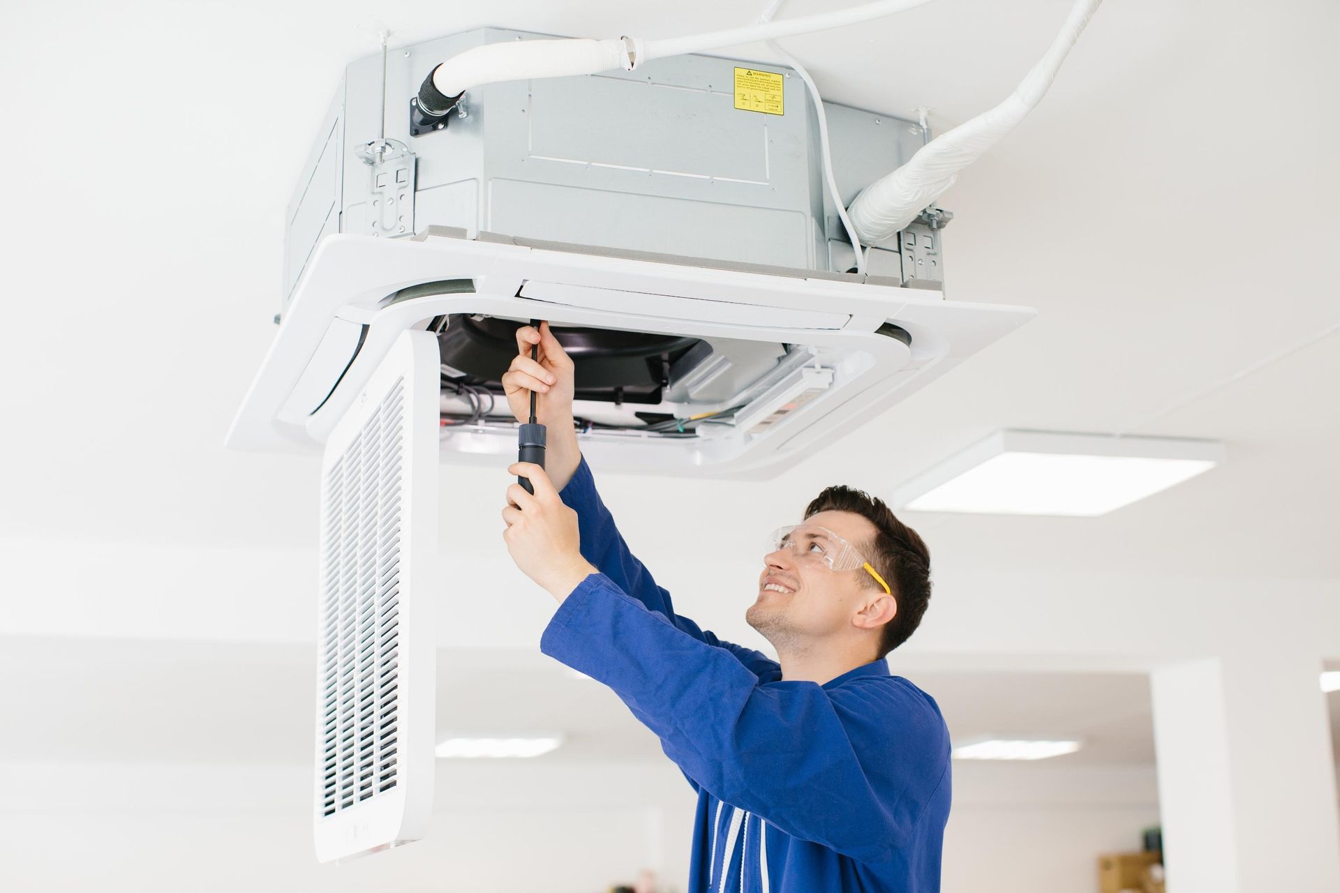 Technician adjusting a ceiling-mounted HVAC unit in a bright office ceiling.