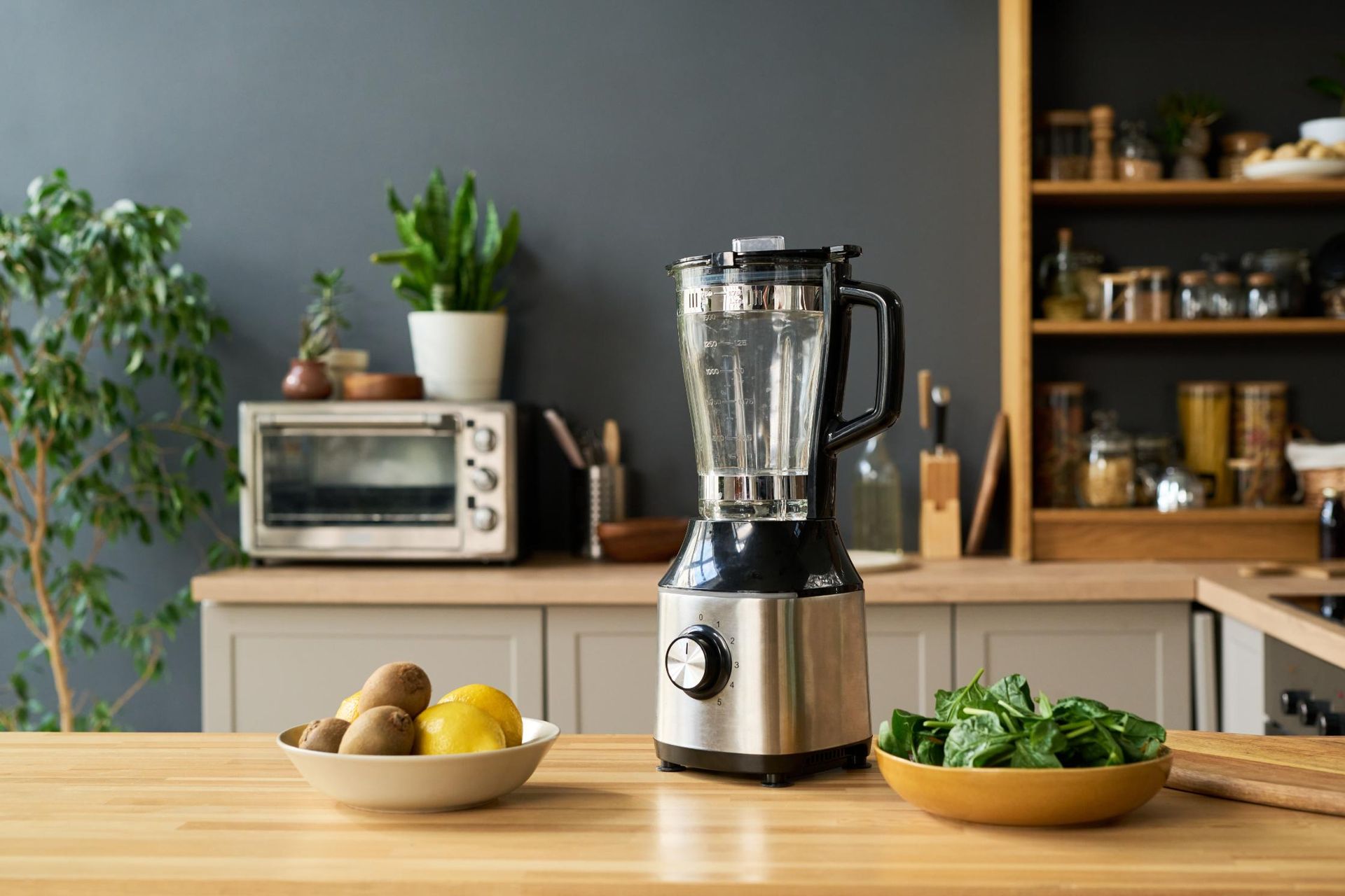 Blender on kitchen counter with bowls of potatoes, lemons, and greens in a bright home kitchen