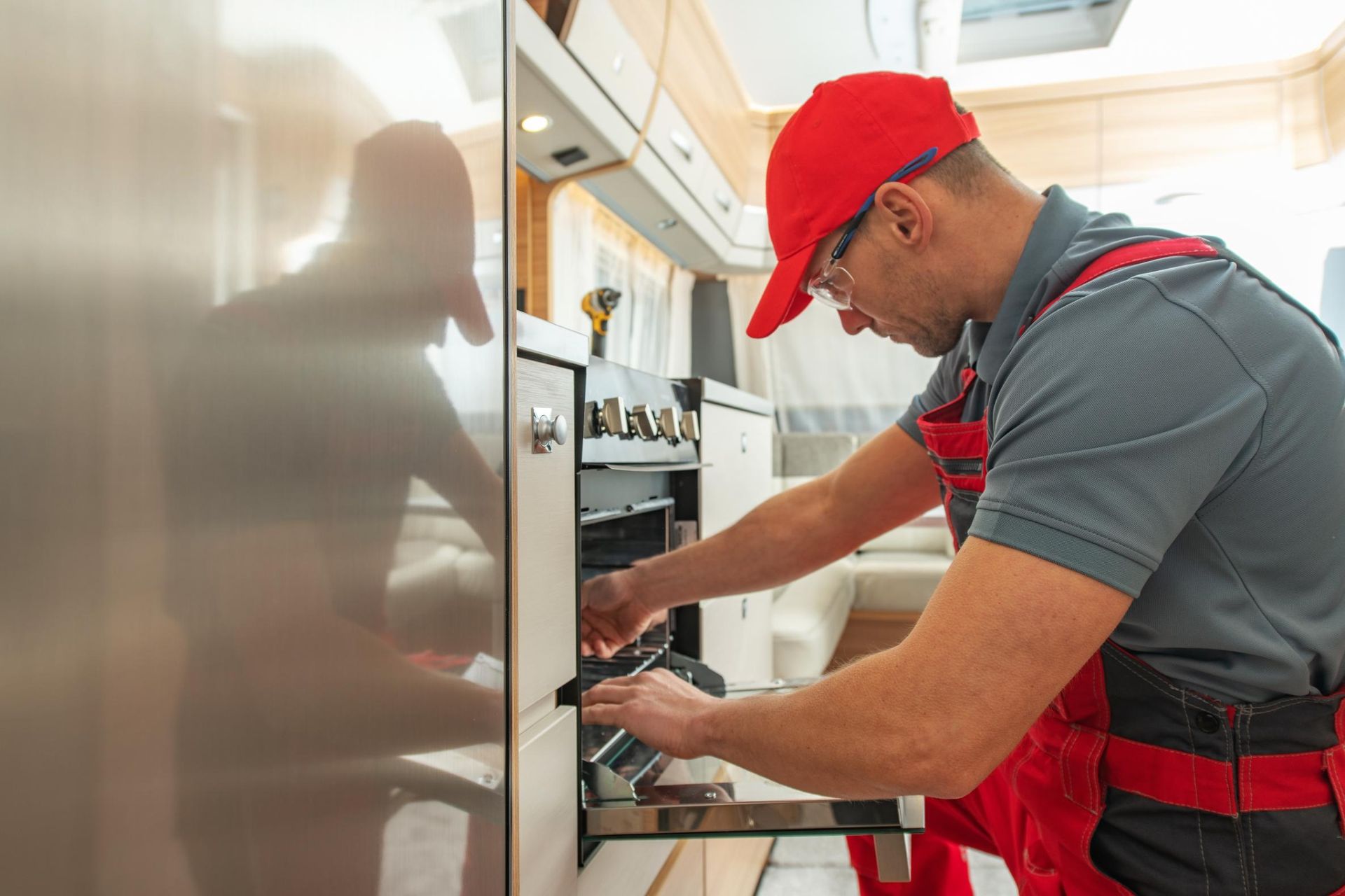 Technician in red cap and apron working on a built-in appliance in a bright kitchen