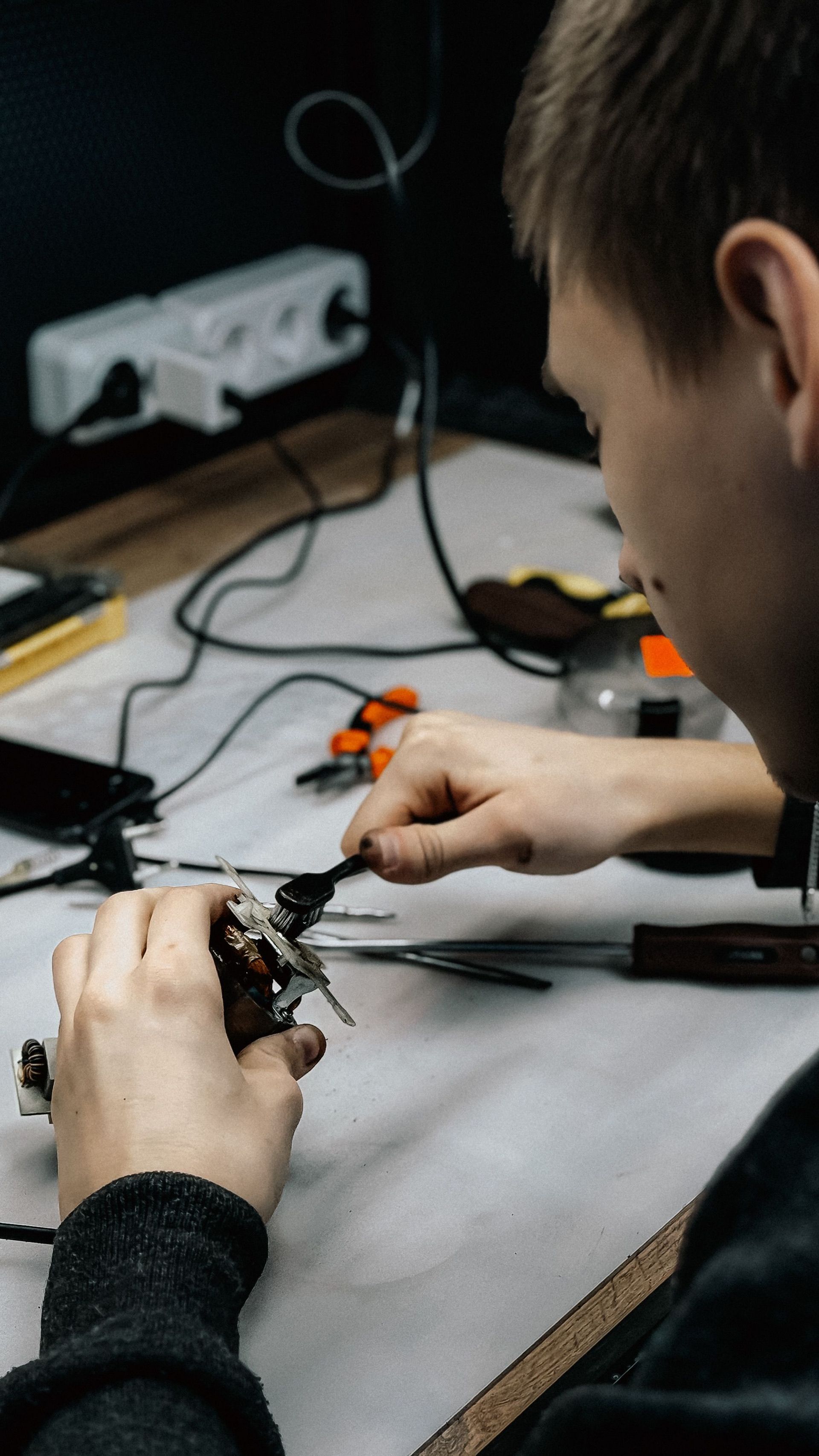 Person soldering electronics on a workbench with tools and wires nearby