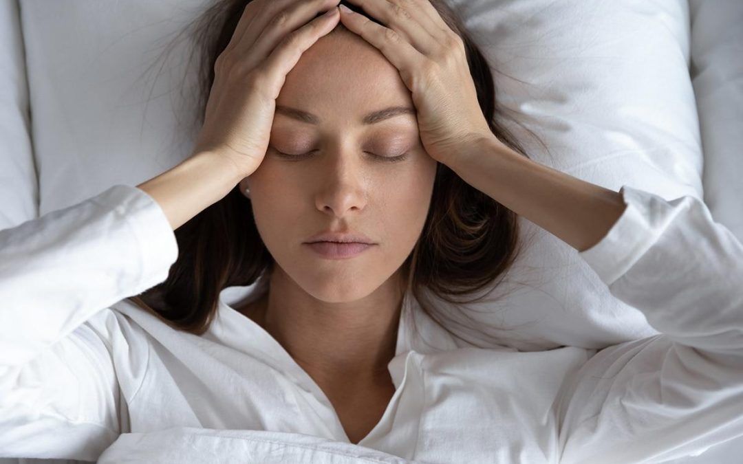 A woman is laying in bed with her hands on her head.