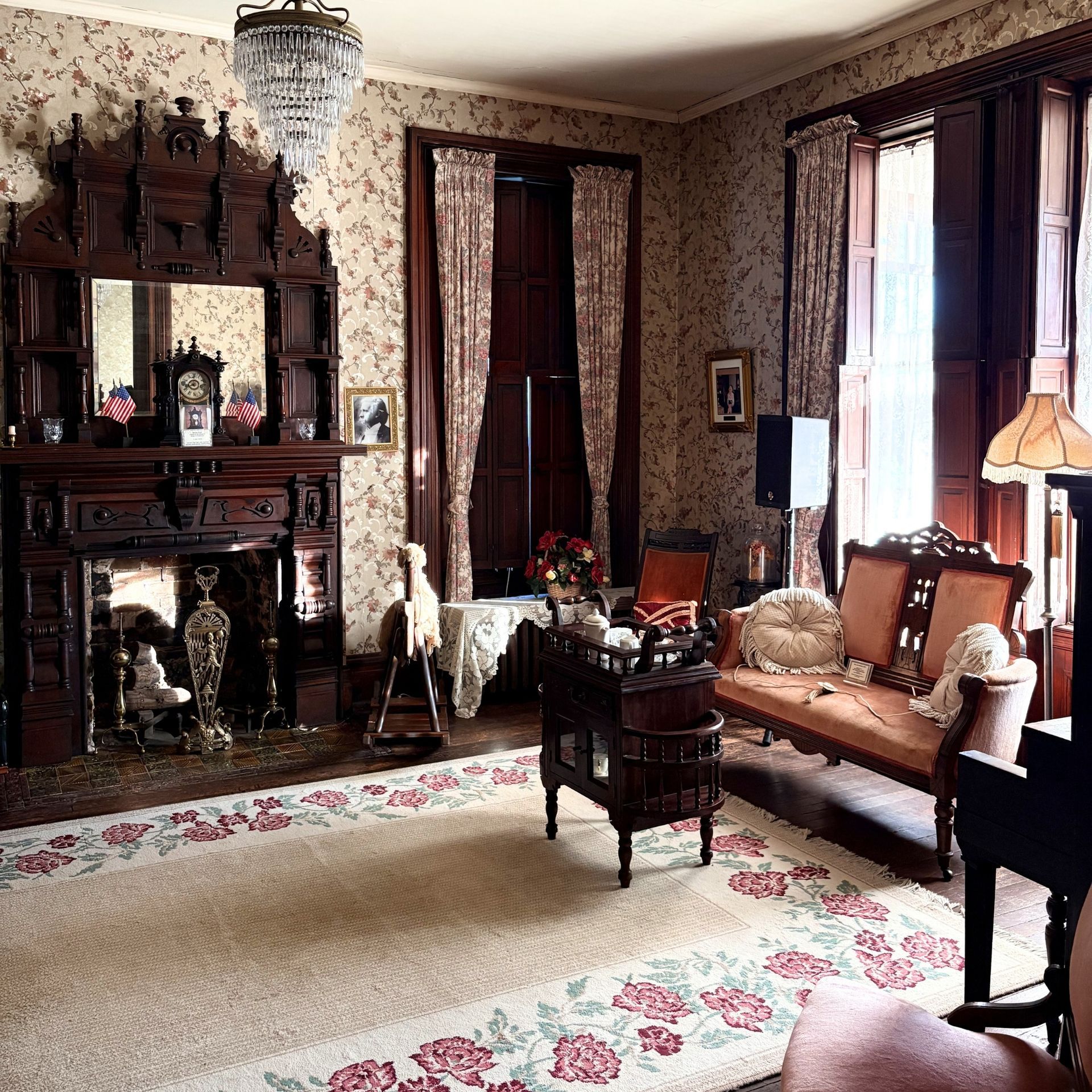 Elegant vintage living room with fireplace, floral wallpaper, chandelier, and antique furniture