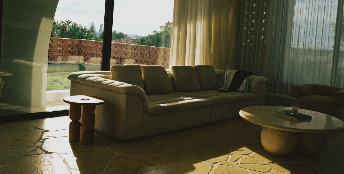 Modern living room with beige sofa, round coffee table, and large sheer curtains by a bright window.