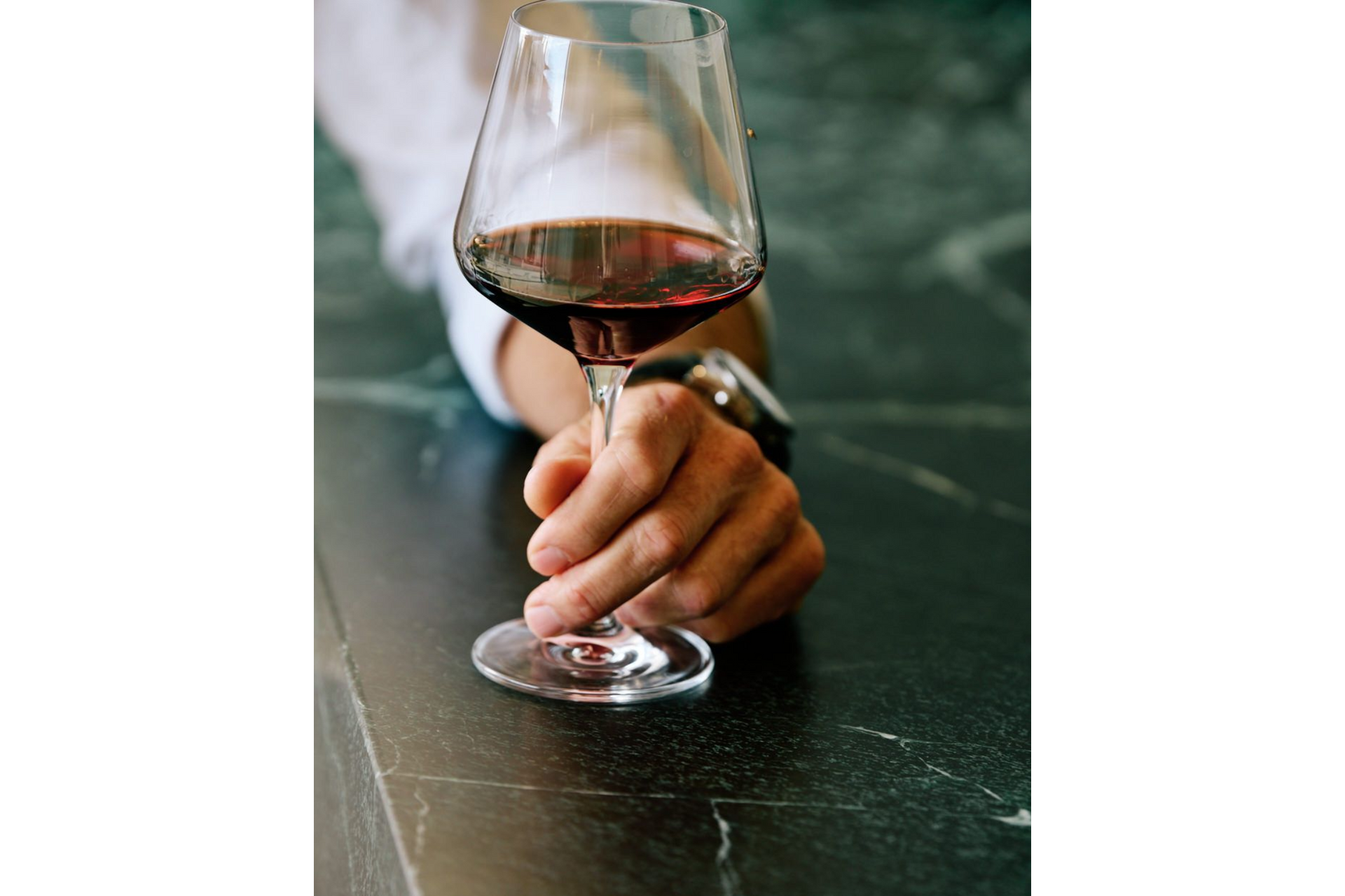 Hand holding a wine glass with red wine on a dark table