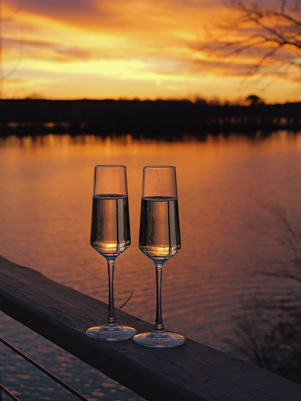 Two champagne flutes on a railing at sunset over calm water