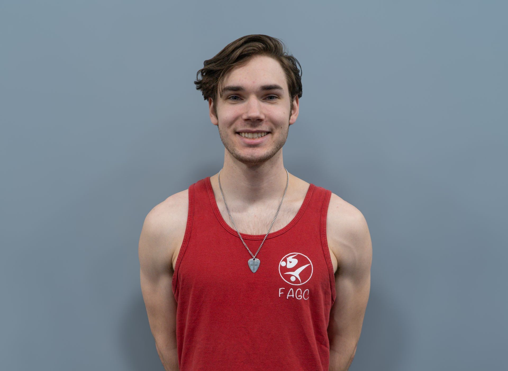 A young man is wearing a red tank top and a necklace.