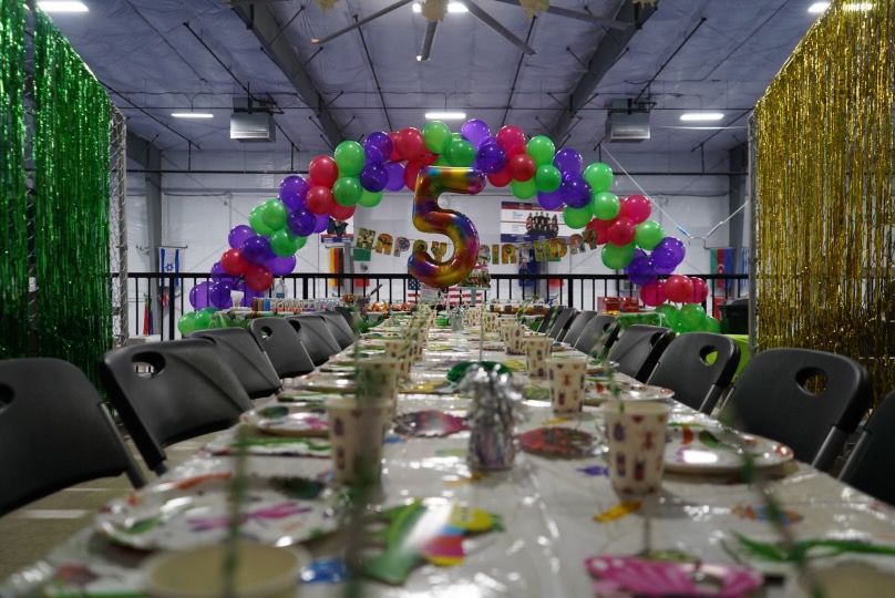 A long table with plates , cups , napkins and a balloon arch for a birthday party.