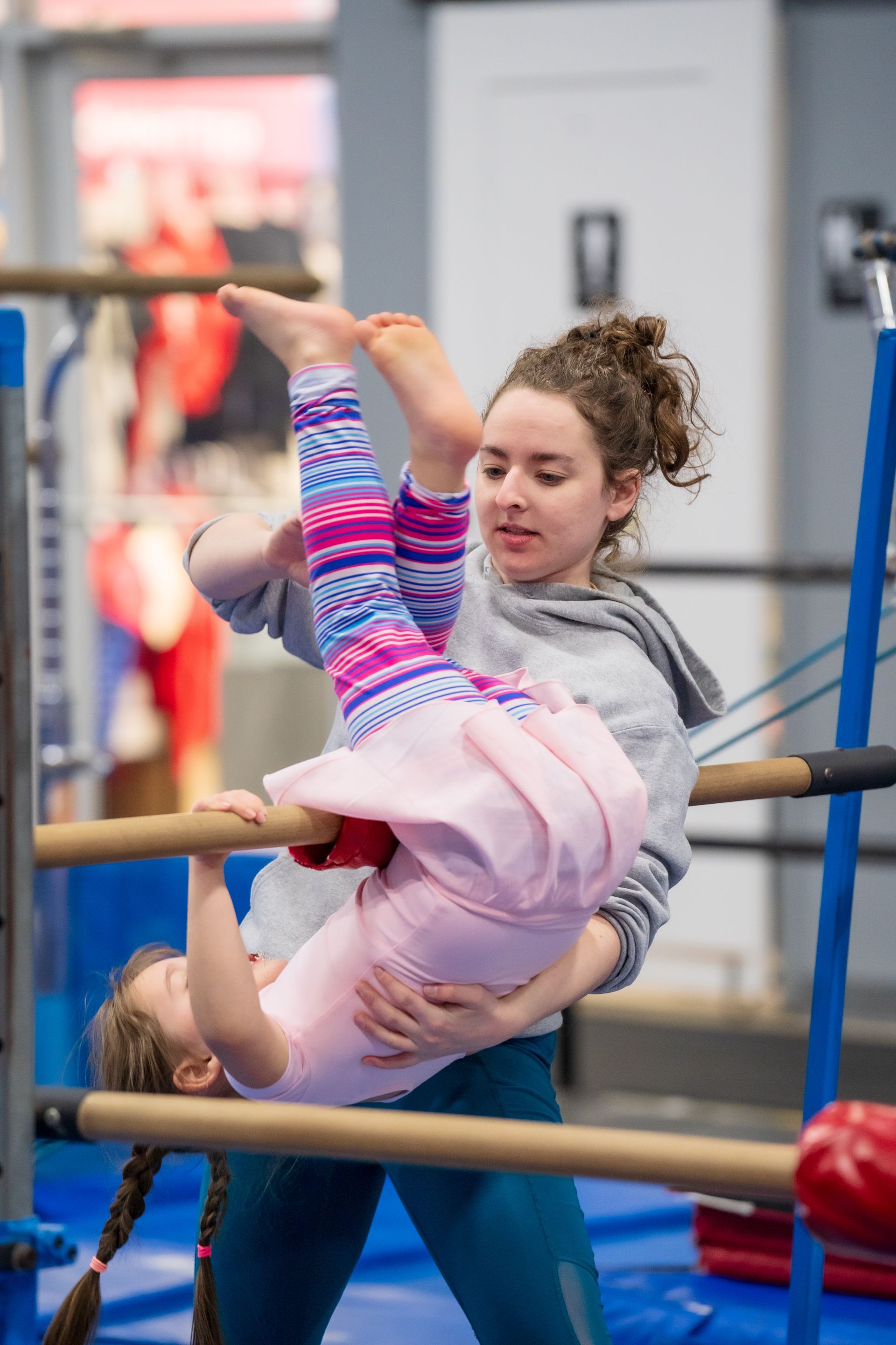 A woman is helping a little girl do a handstand on a bar.