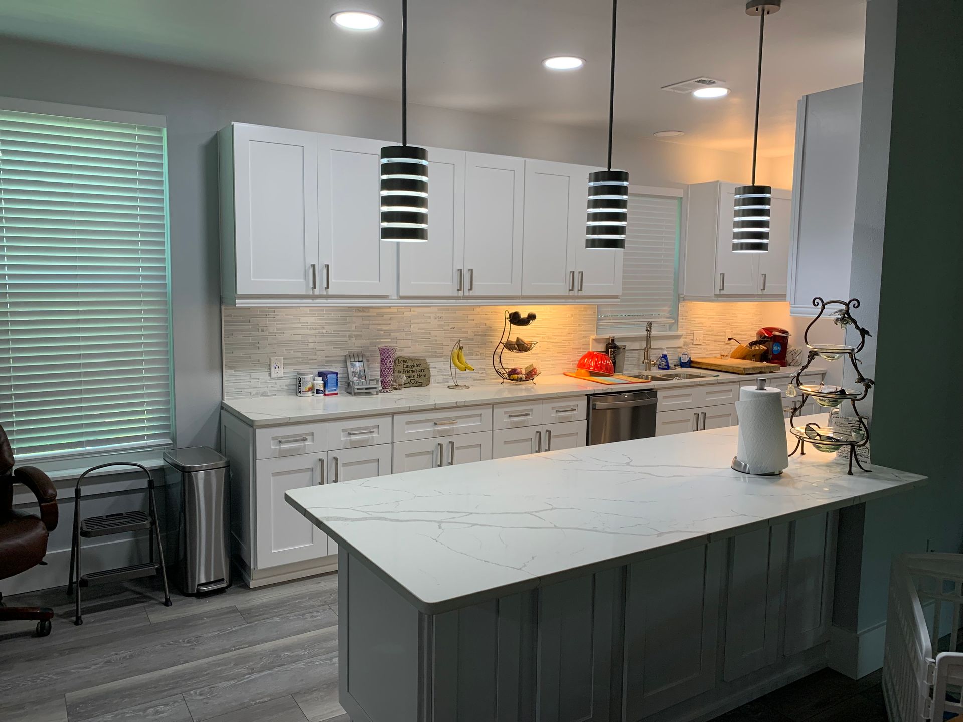 Modern kitchen with white cabinets, gray island, pendant lights, and a large window with blinds