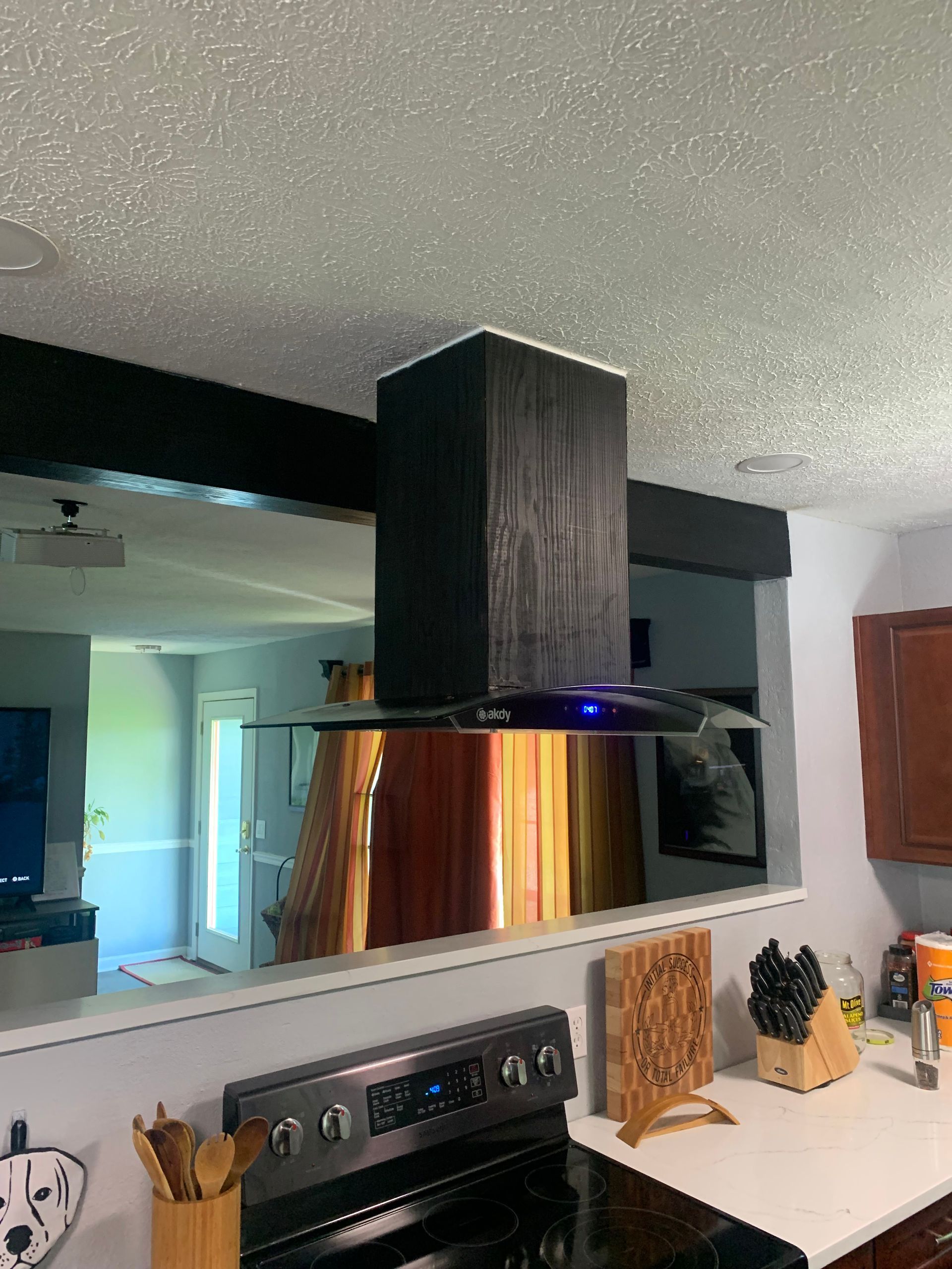 Kitchen with black range hood over stove, white countertops, and a mirrored backsplash reflecting the room.