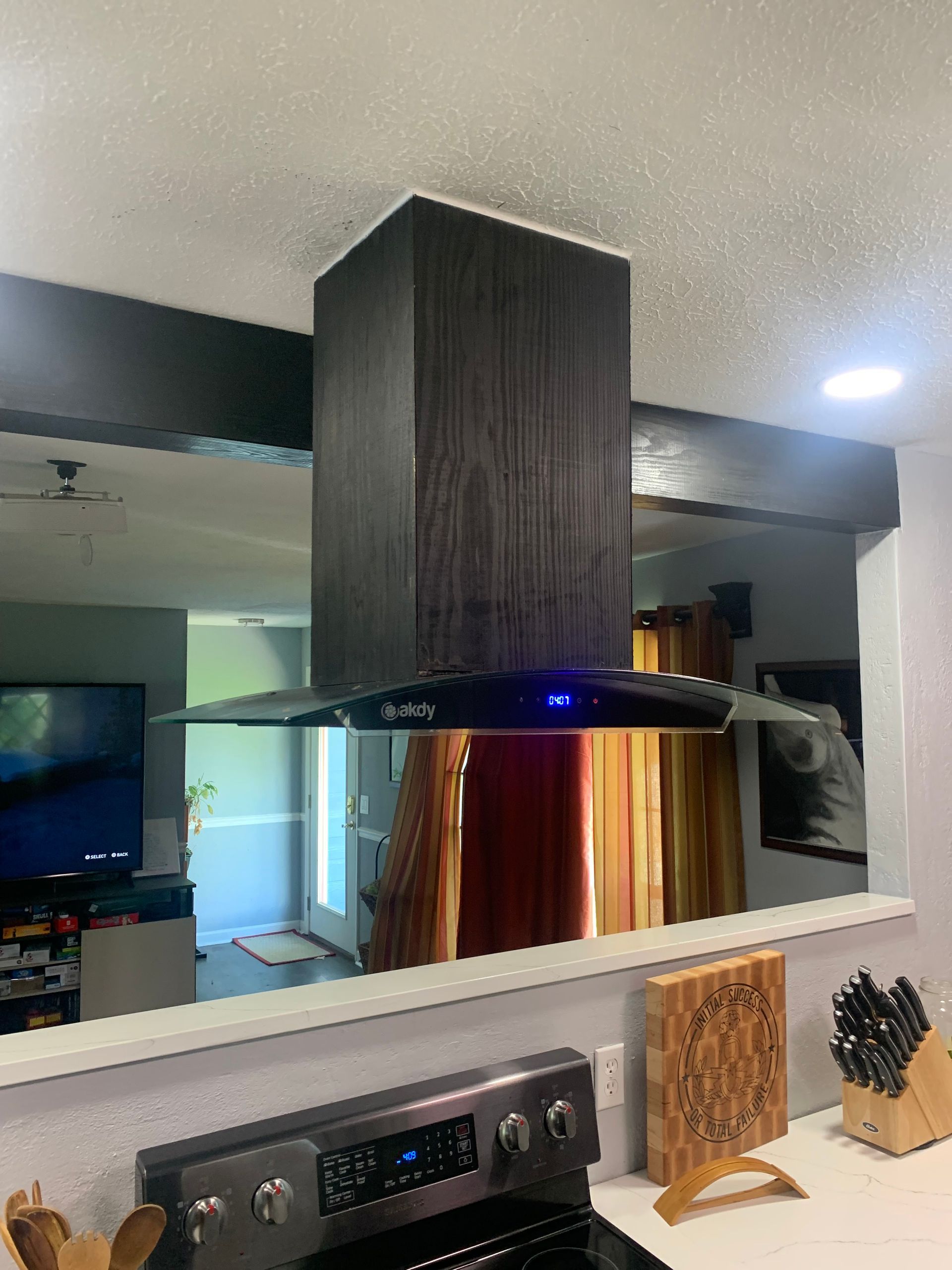 Modern kitchen with a black range hood above a stainless stove and wooden cabinet paneling